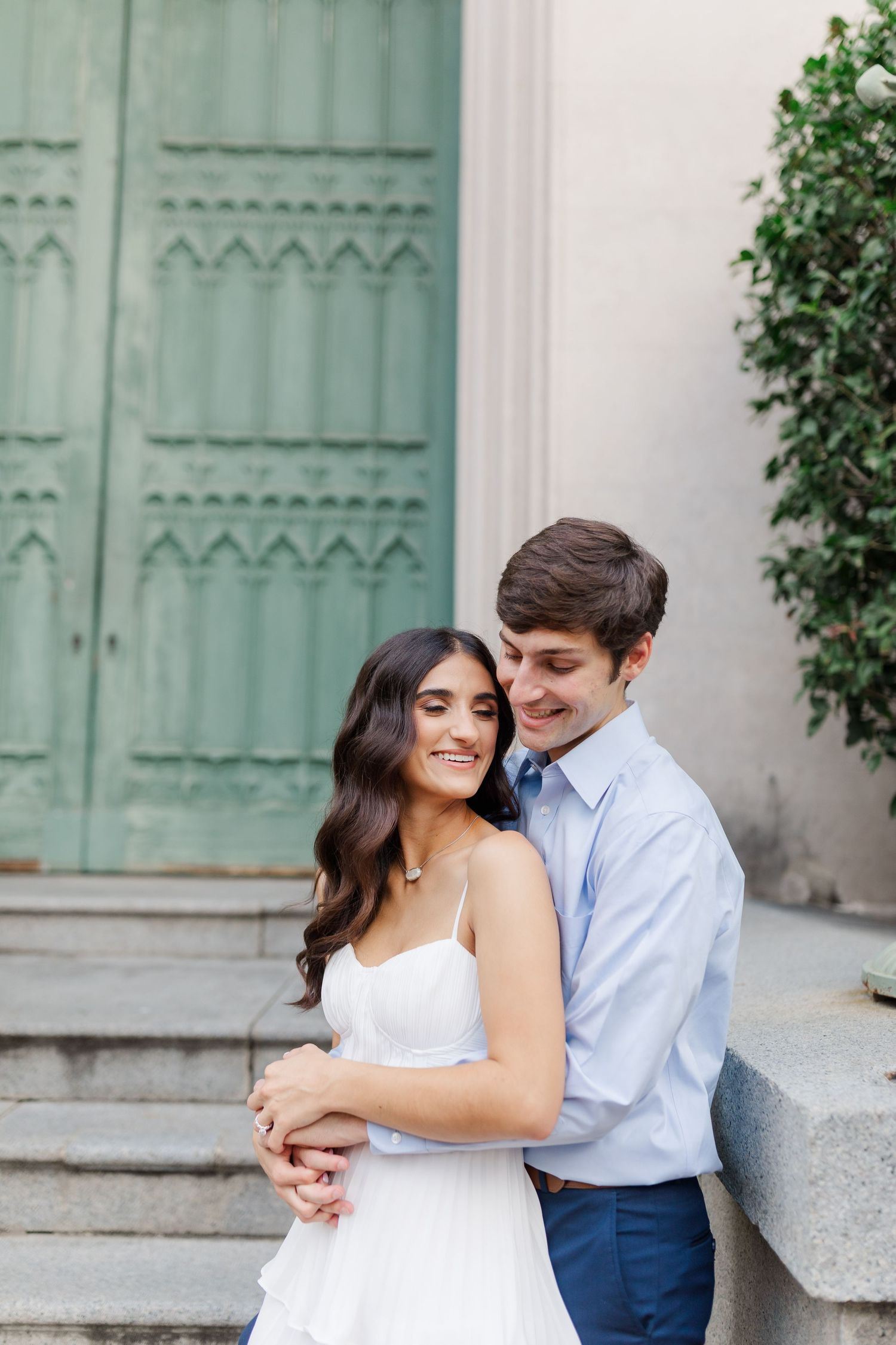 A romantic couple embraces on stone steps in front of a vintage mint green door with decorative details.
