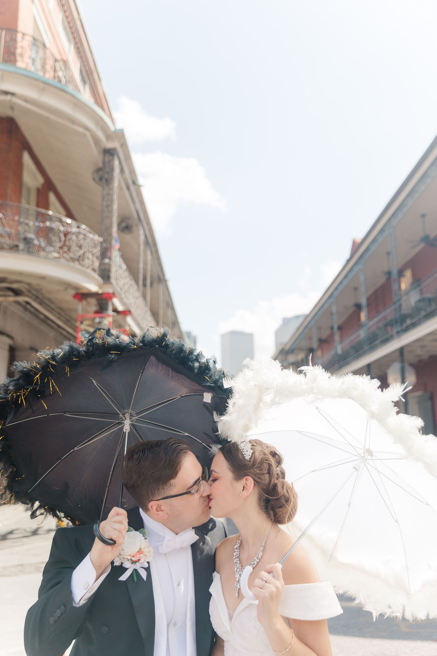 Wedding couple with parasols sharing kiss on historic New Orleans street.