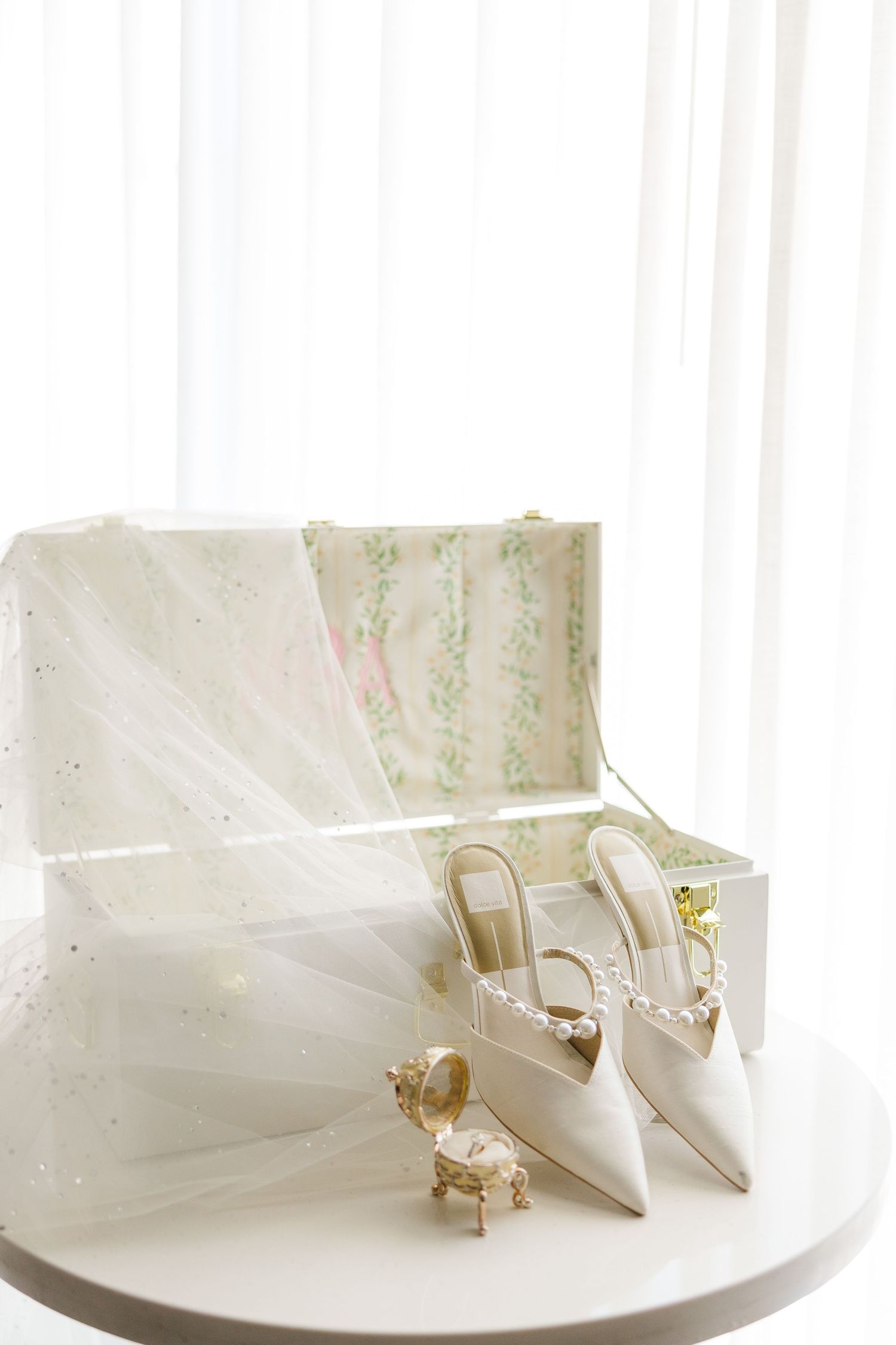 Elegant white bridal shoes and veil displayed in a decorative box against white backdrop.