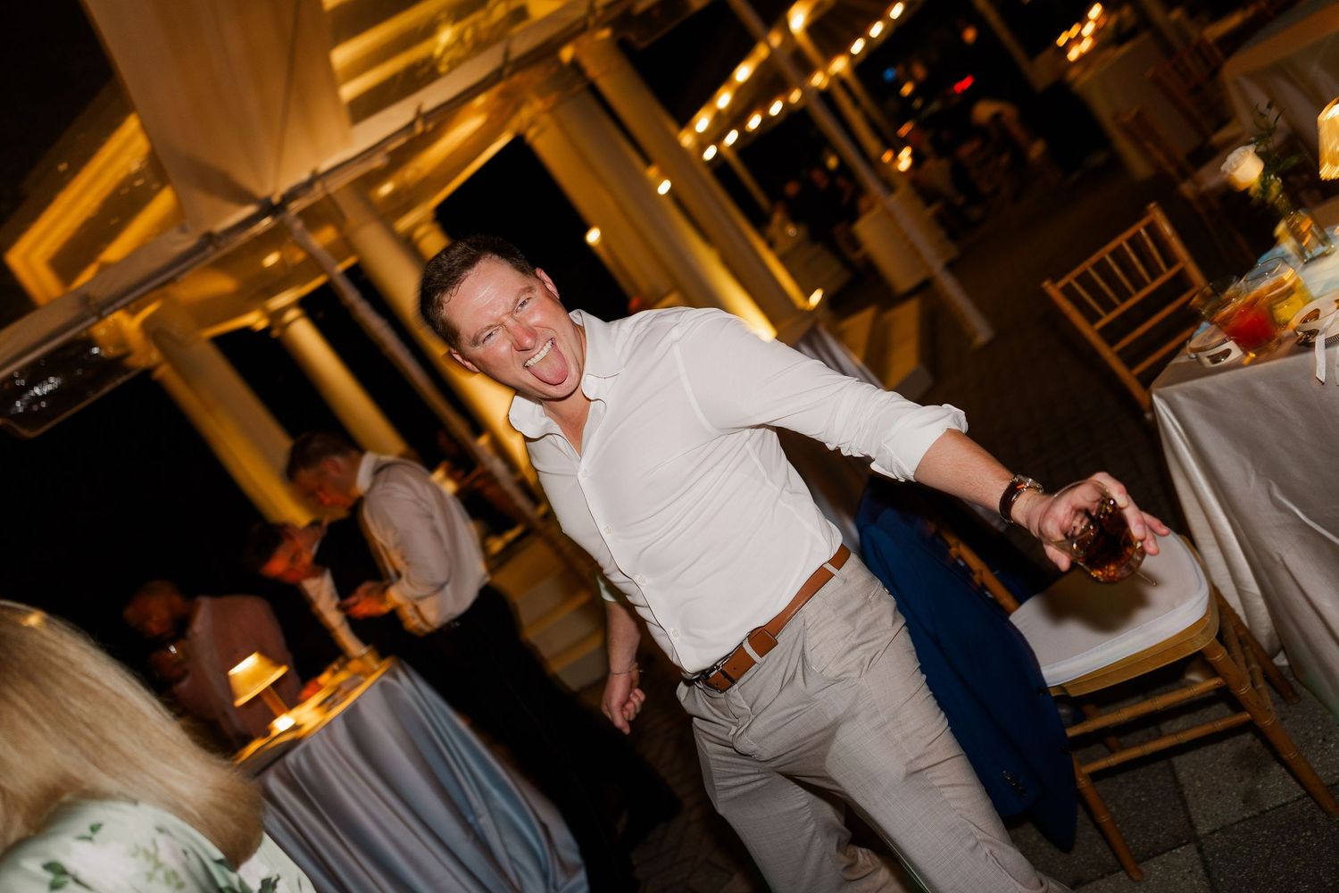 A guest dances joyfully at an evening wedding reception with warm lighting and decorative elements.