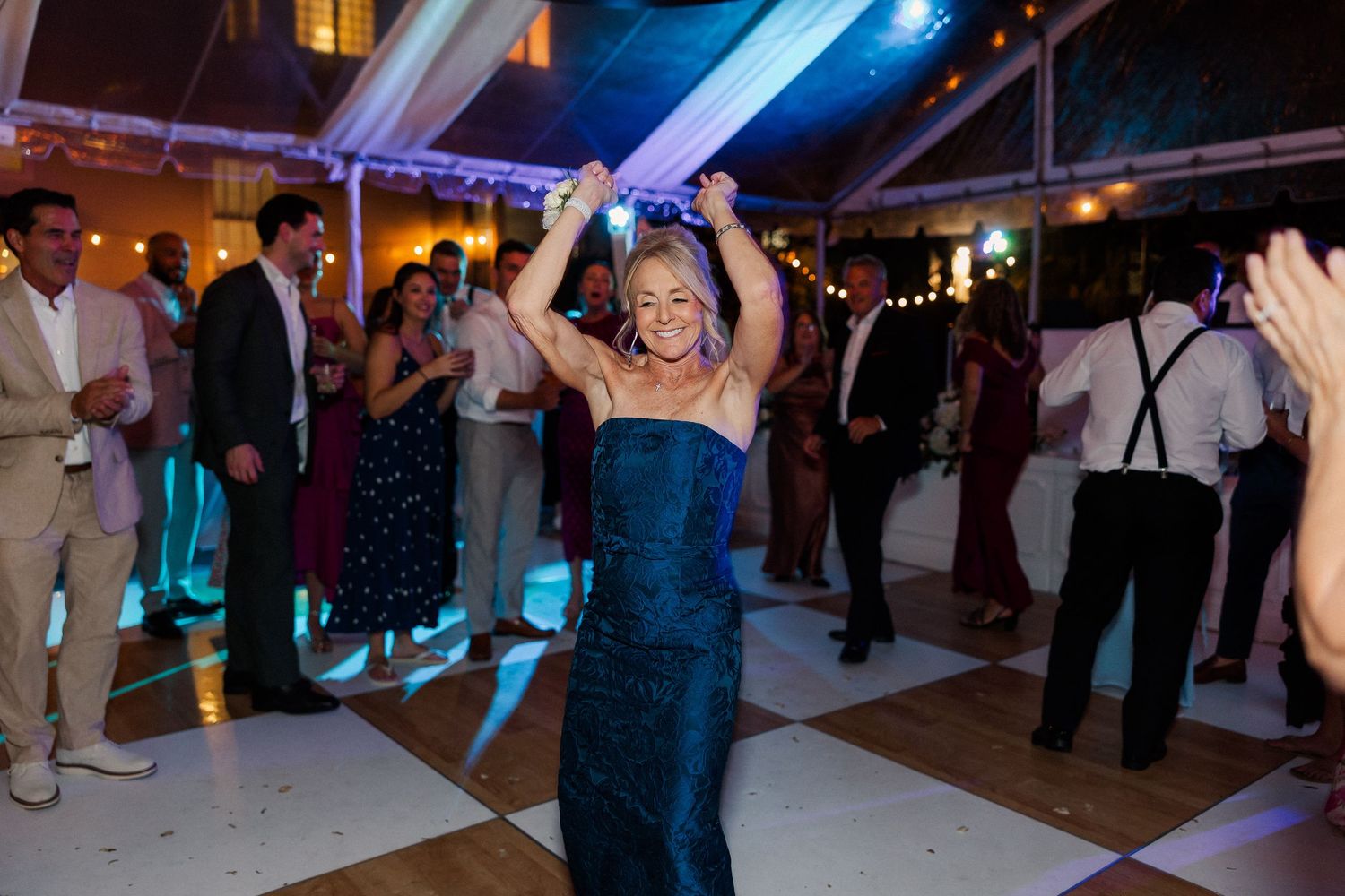 Wedding guests dancing and celebrating on a dimly lit dance floor under string lights.