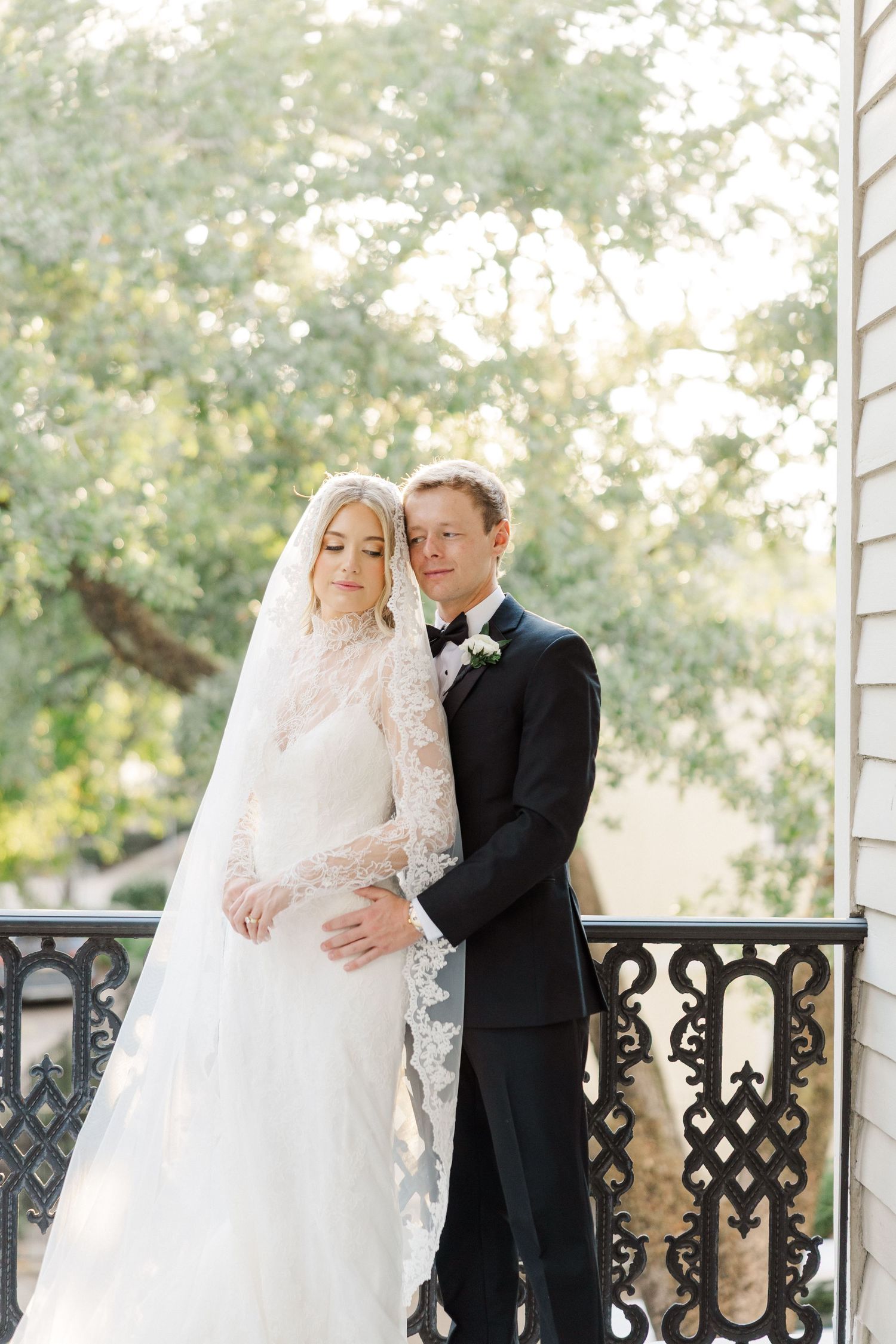 A romantic wedding couple shares intimate moments on an elegant porch with ornate black railings.