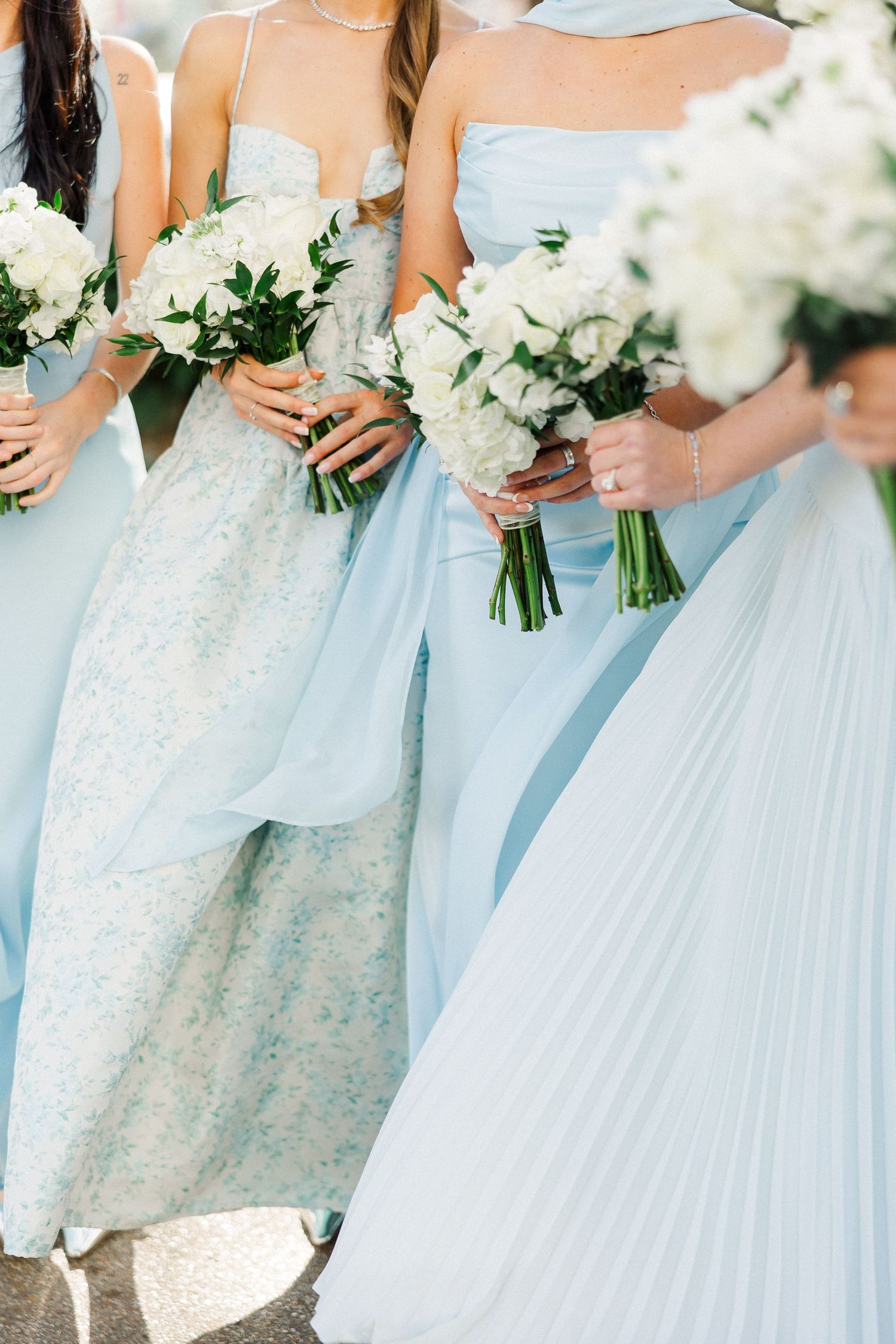 Bridesmaids in light blue dresses hold white floral bouquets at an elegant wedding ceremony.