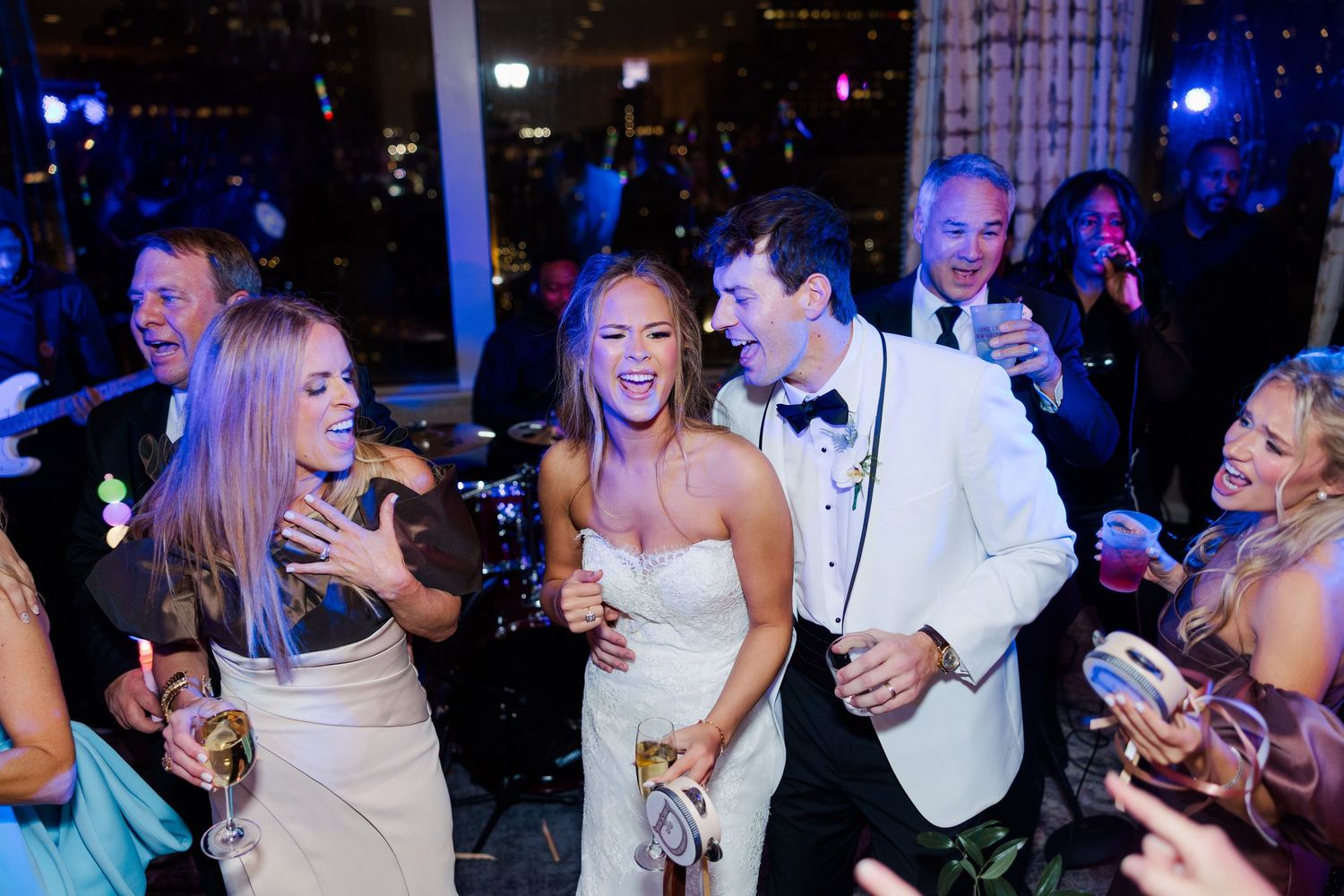 Wedding guests dancing and celebrating at a lively reception with blue lighting.
