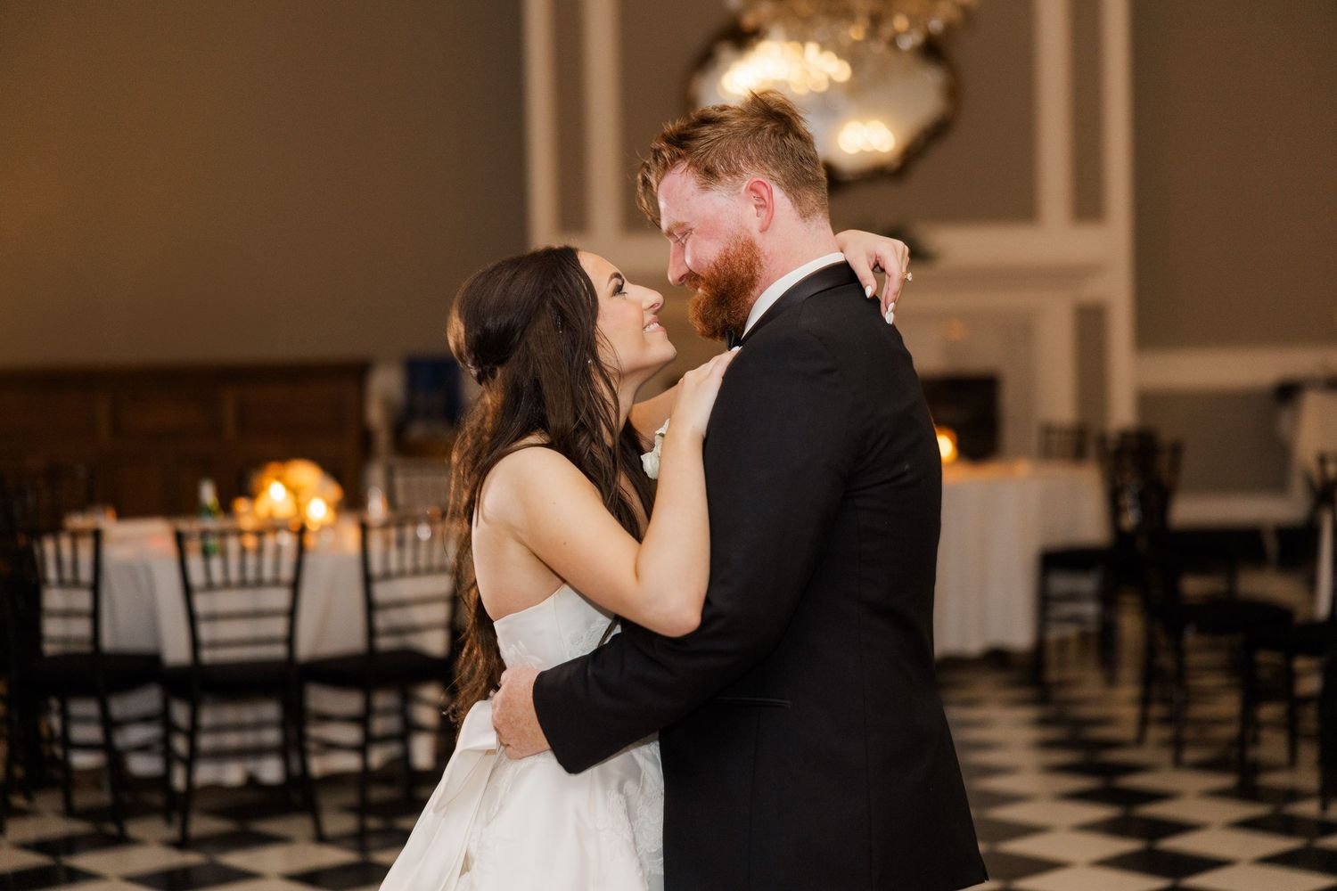 Romantic dance between newlyweds in elegant ballroom with checkerboard flooring.