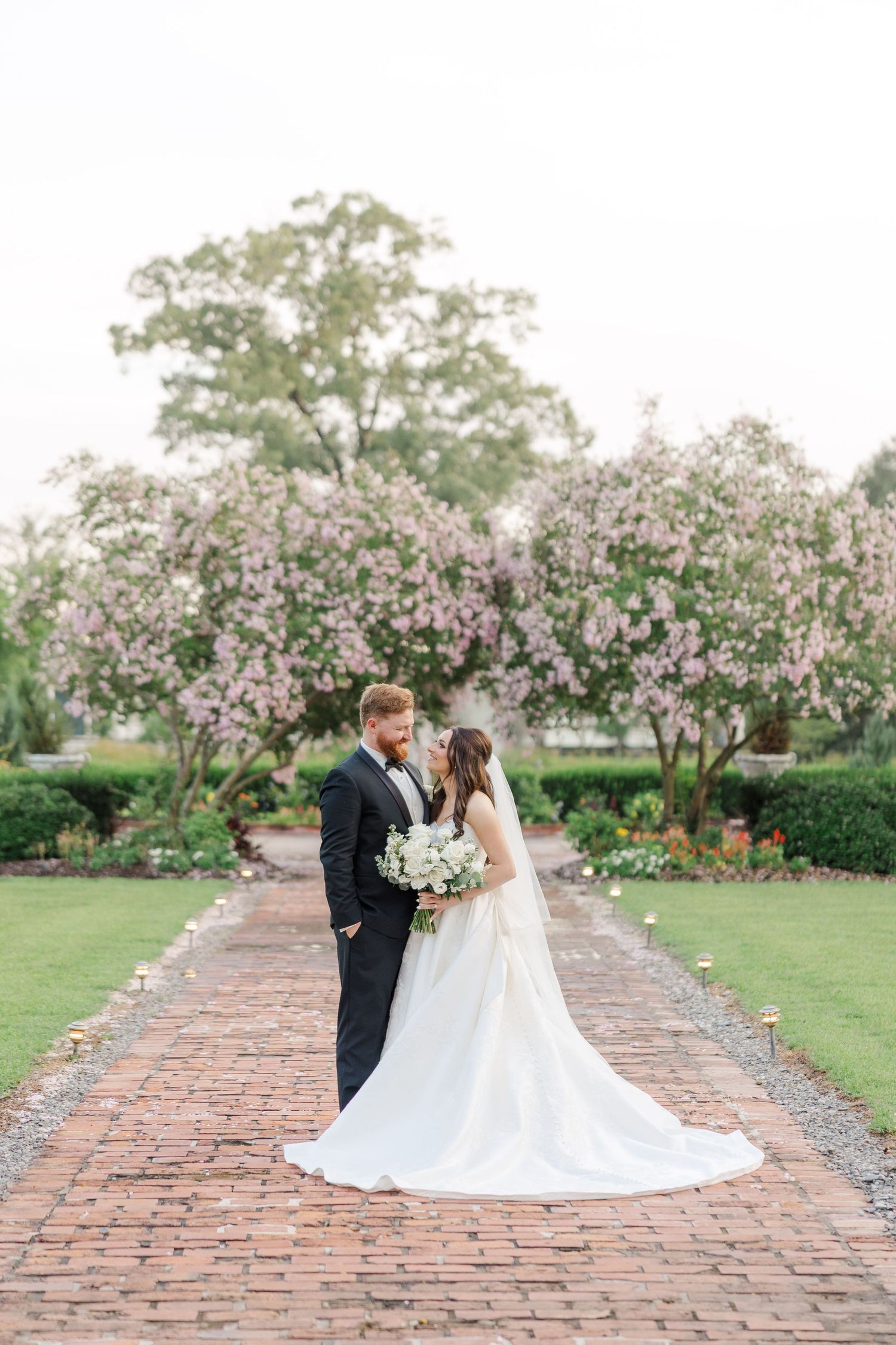 Wedding couple walking along a brick path surrounded by blooming spring trees and gardens.