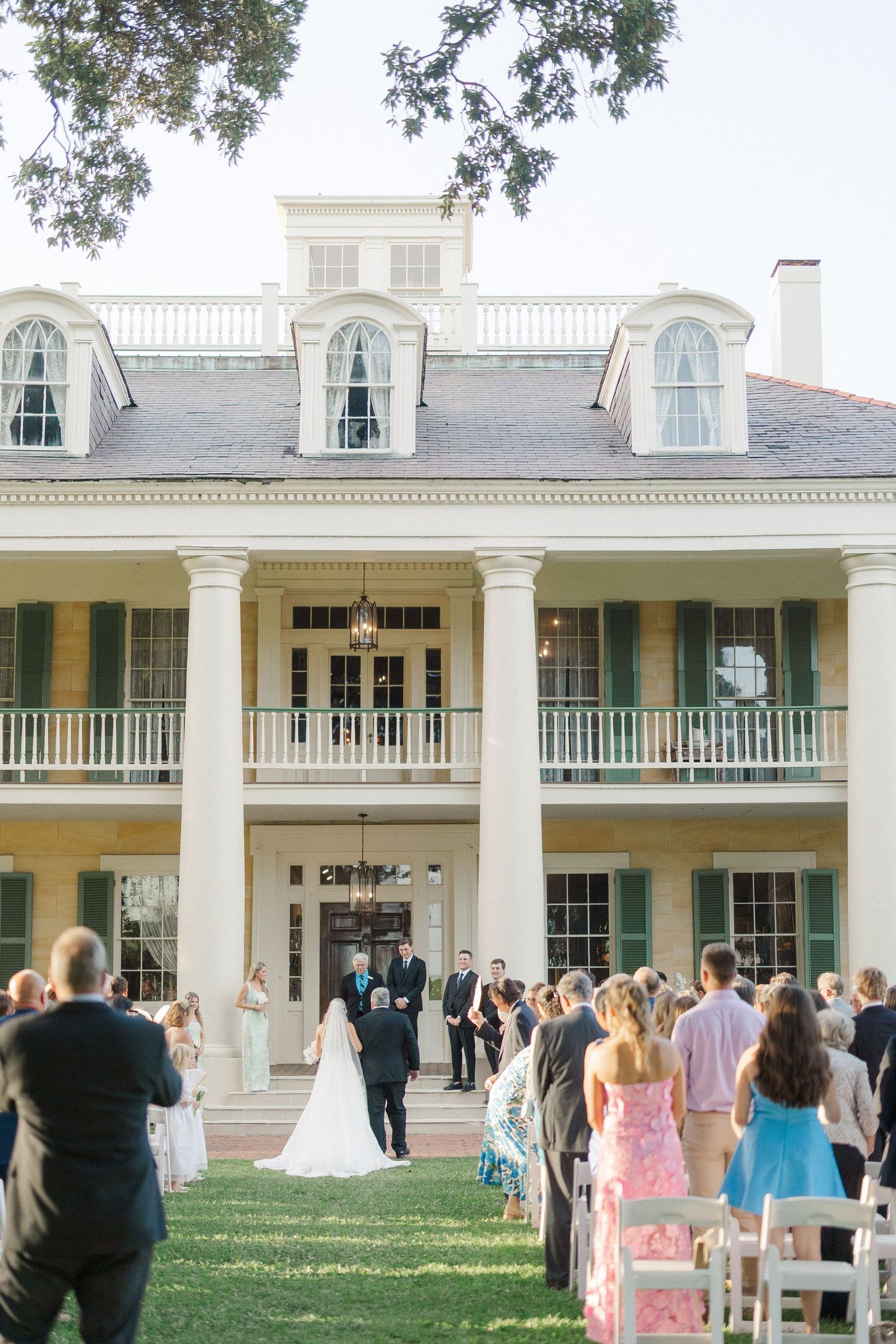 Outdoor wedding ceremony on the lawn of an elegant Southern plantation-style mansion.