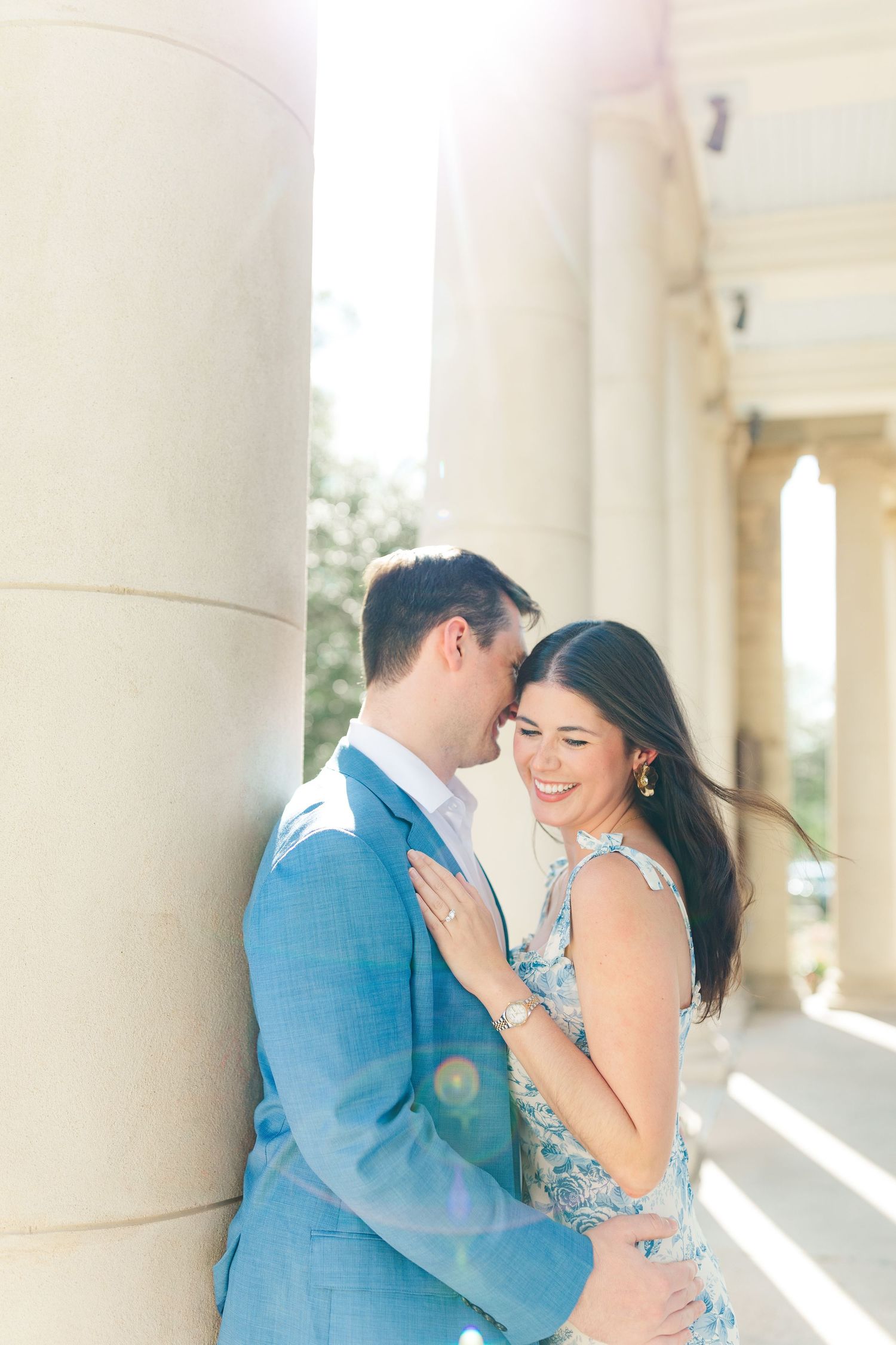 A romantic couple embraces in front of elegant white columns during a sunlit outdoor photo session.