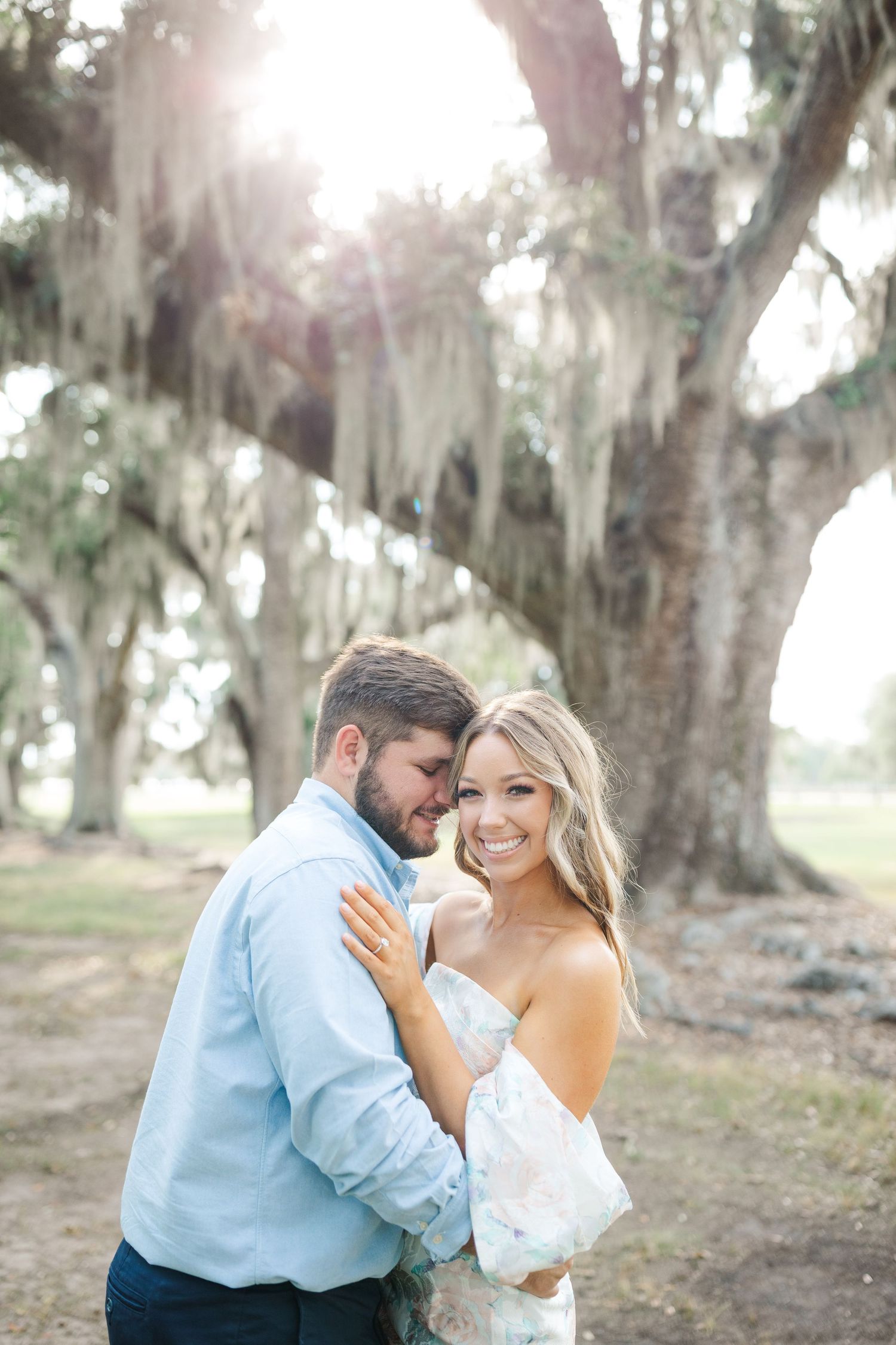 A couple shares an intimate moment beneath moss-draped oak trees in a dreamy outdoor setting.