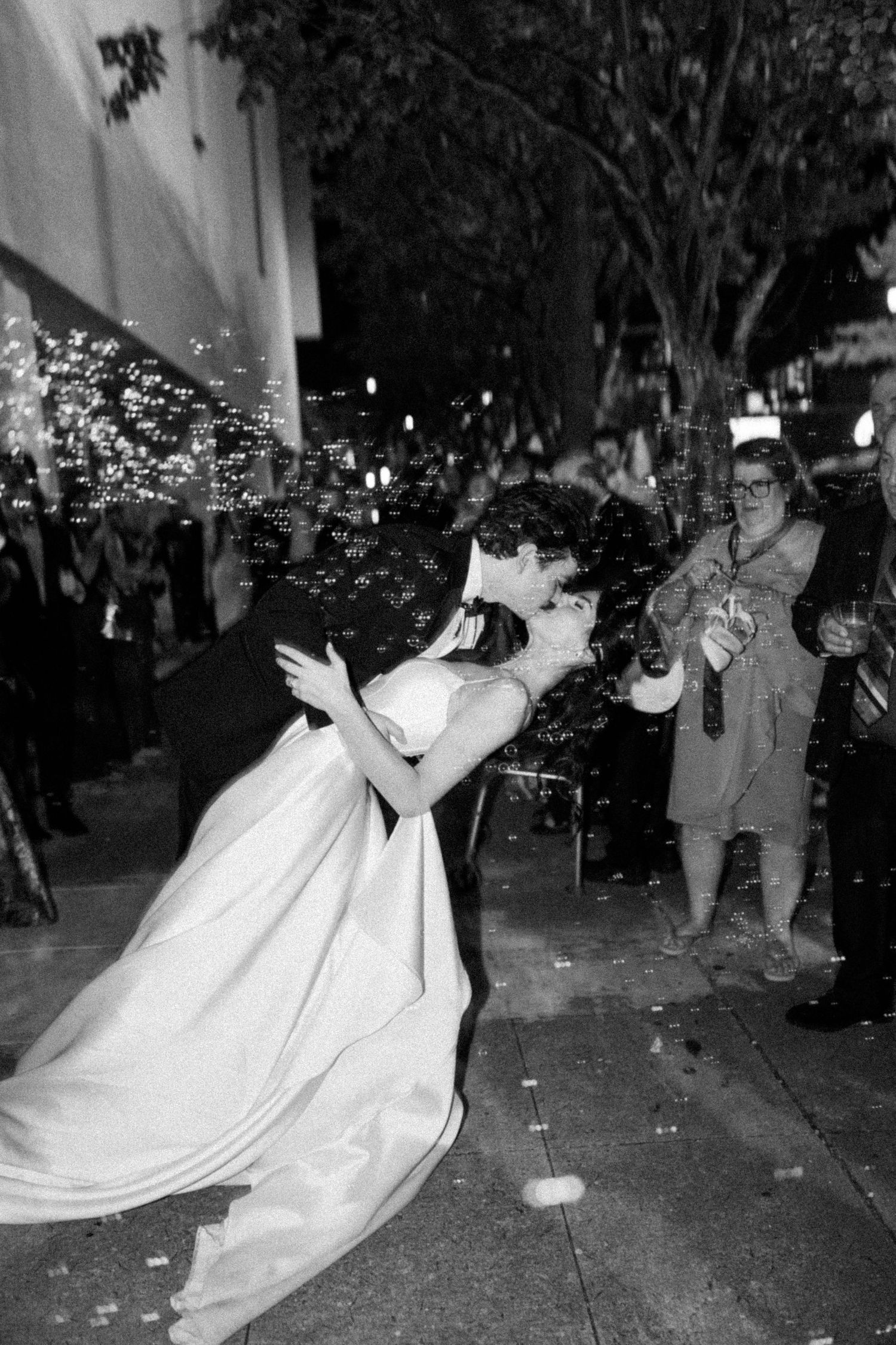 Groom dipping bride for romantic kiss outside at night in black and white photo.