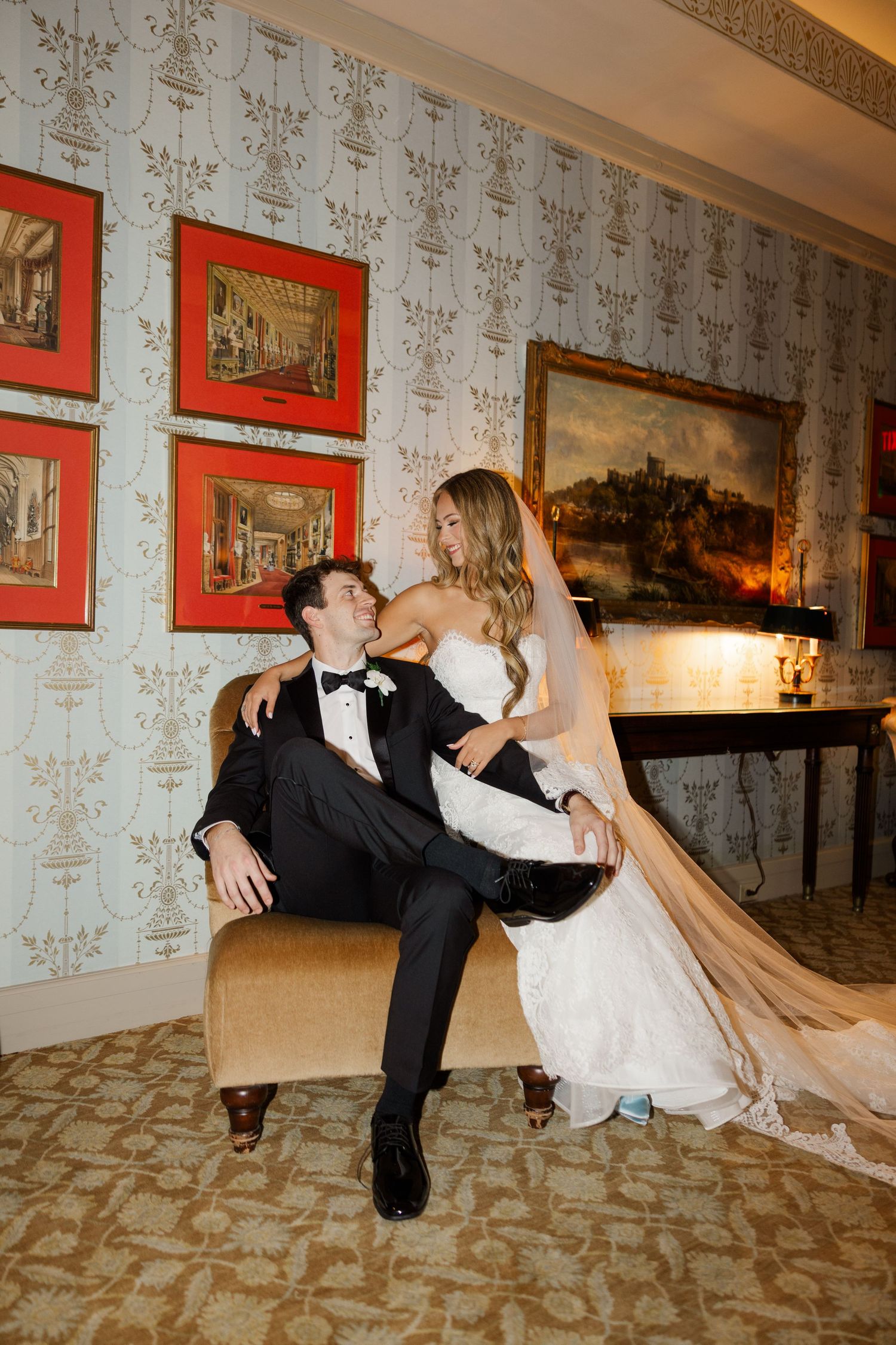 Romantic wedding couple performs dramatic dip dance move in elegant room with vintage wallpaper and red framed artwork.