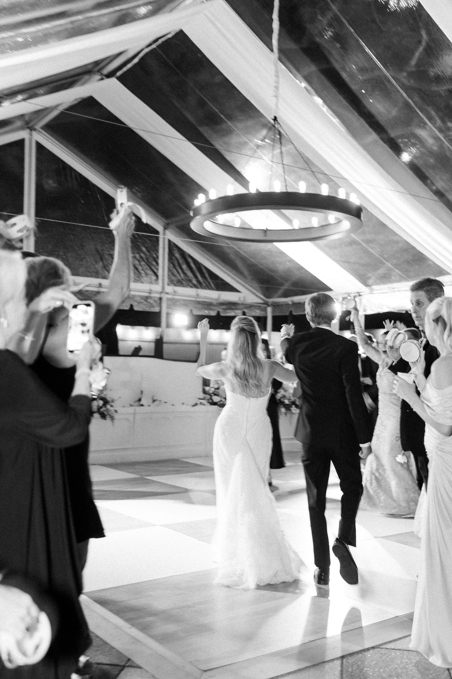 Wedding couples dancing in an elegant white-themed reception venue with dramatic lighting.
