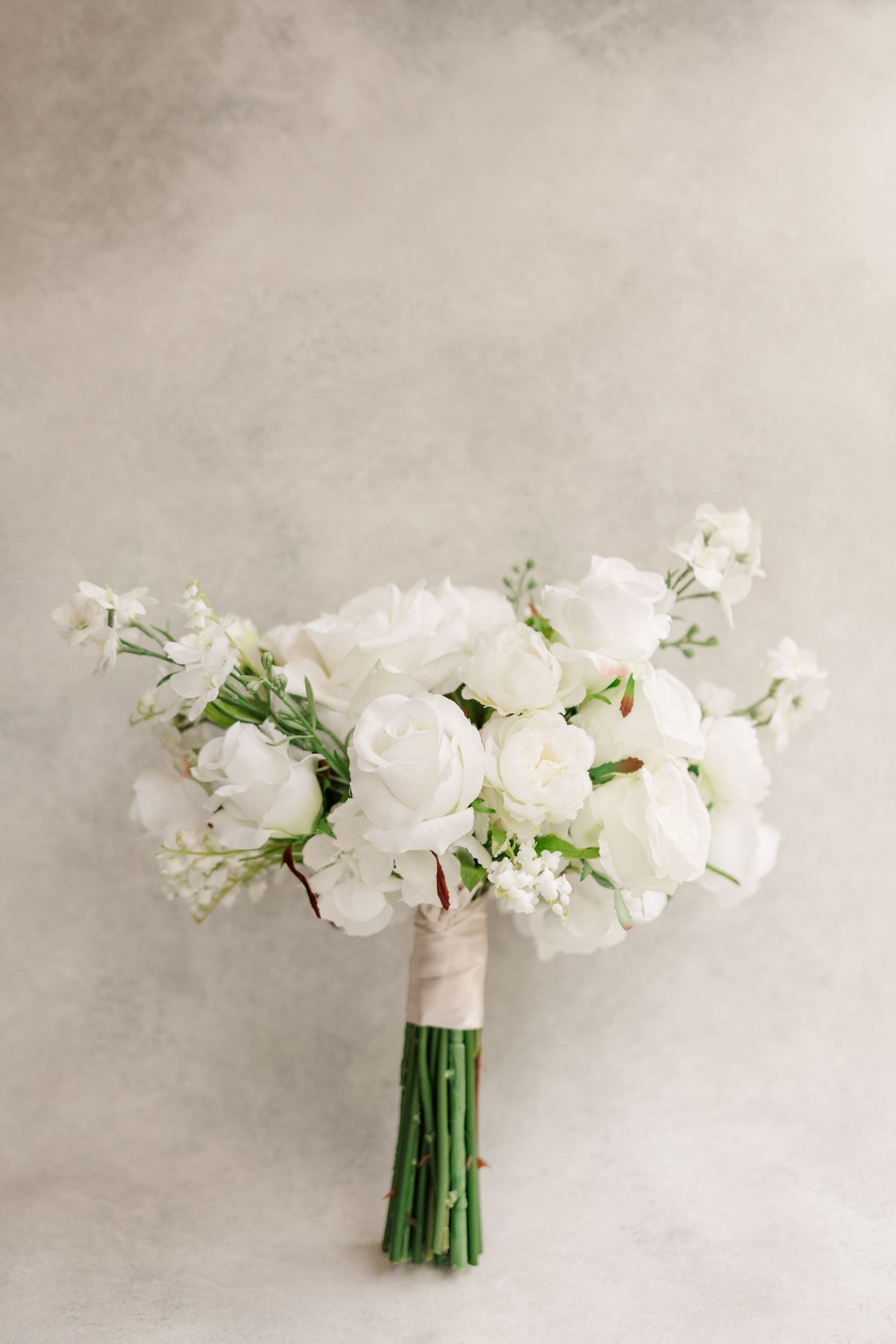 White floral bouquet with roses and greenery arranged in an elegant display against a neutral background.