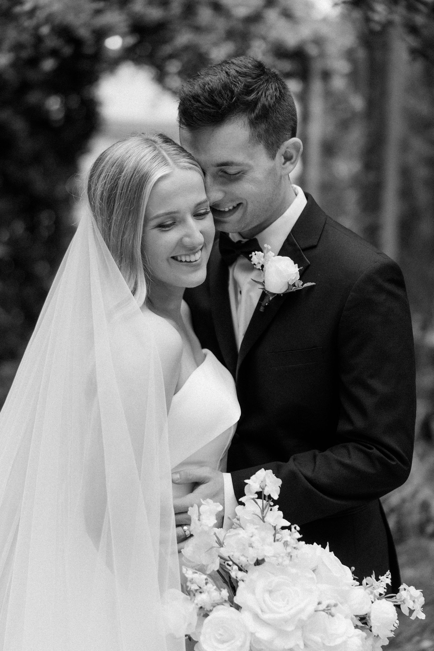 Black and white portrait of newlyweds sharing an intimate moment with white floral bouquet.