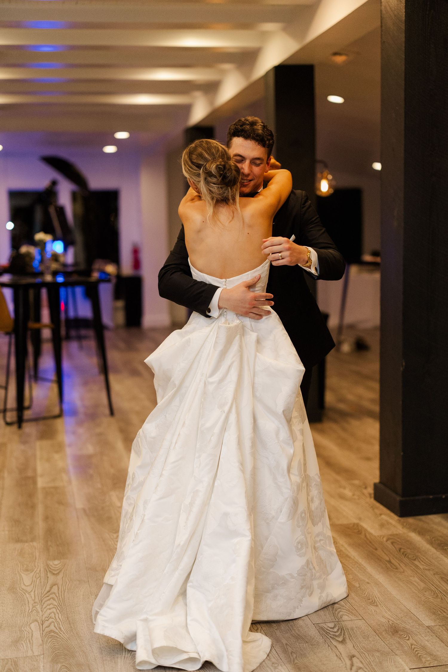 Couple shares their first dance in an elegant reception venue with modern lighting and wood floors.