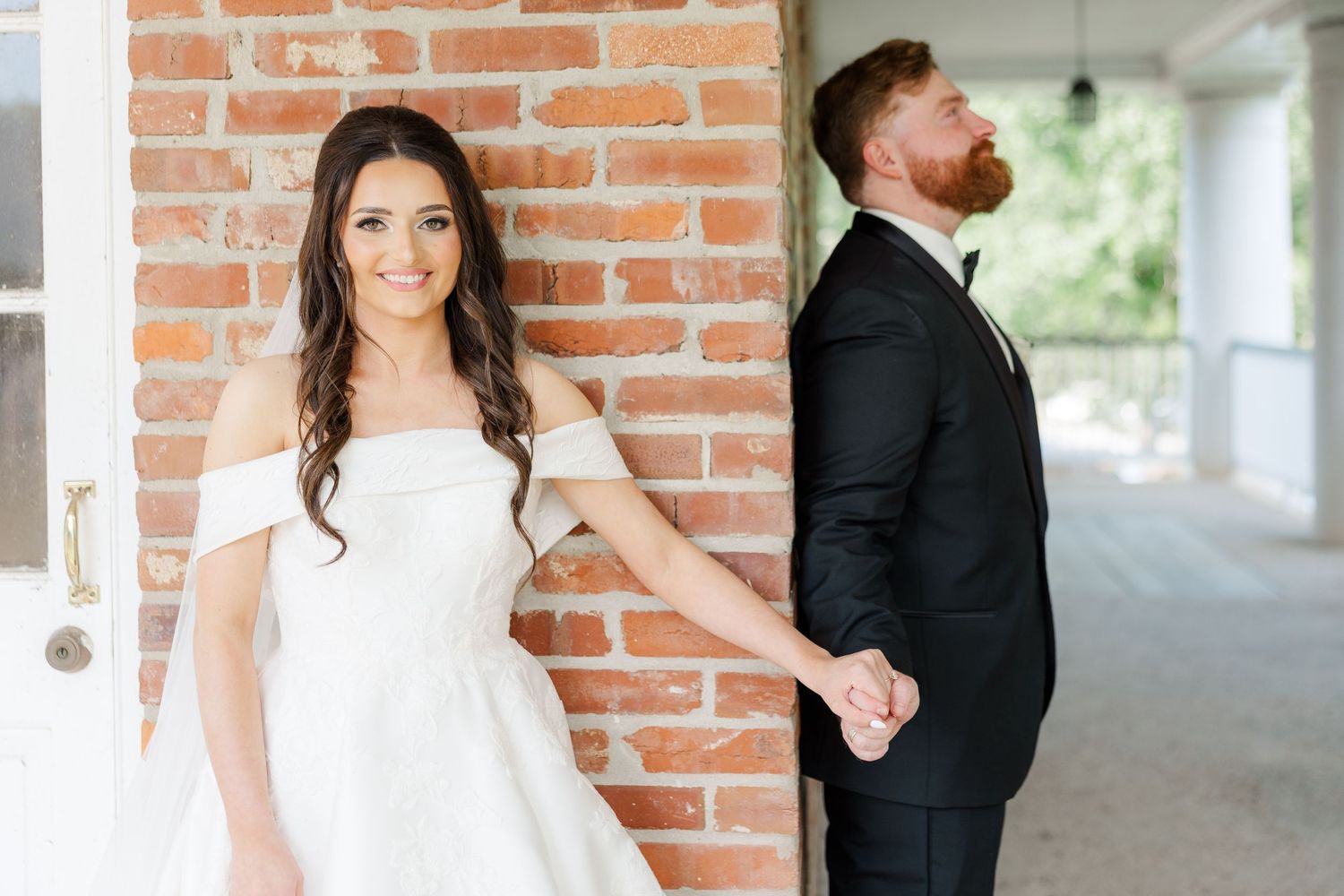 Wedding couple poses in front of rustic brick wall in outdoor covered walkway.
