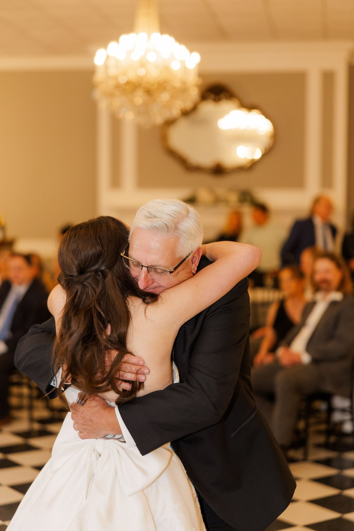 A heartwarming father-daughter dance at an elegant wedding reception with chandeliers overhead.