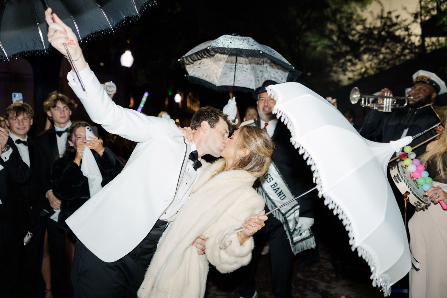 Wedding celebration with guests dancing and holding parasols at night.