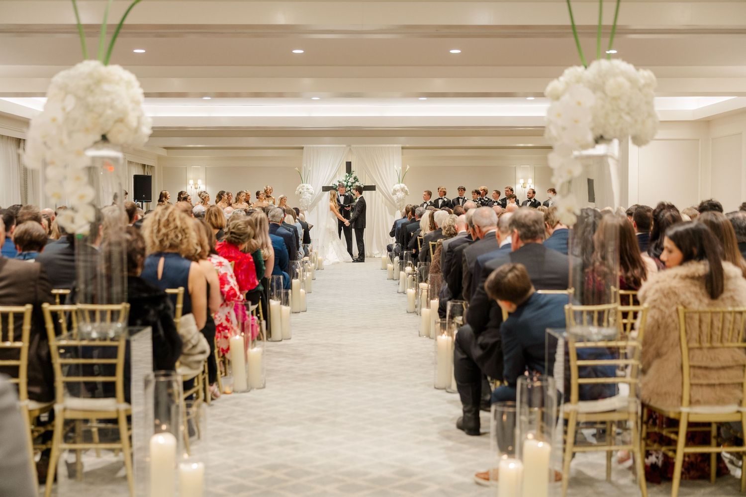 Elegant wedding reception hall setup with gold chairs and white floral arrangements.
