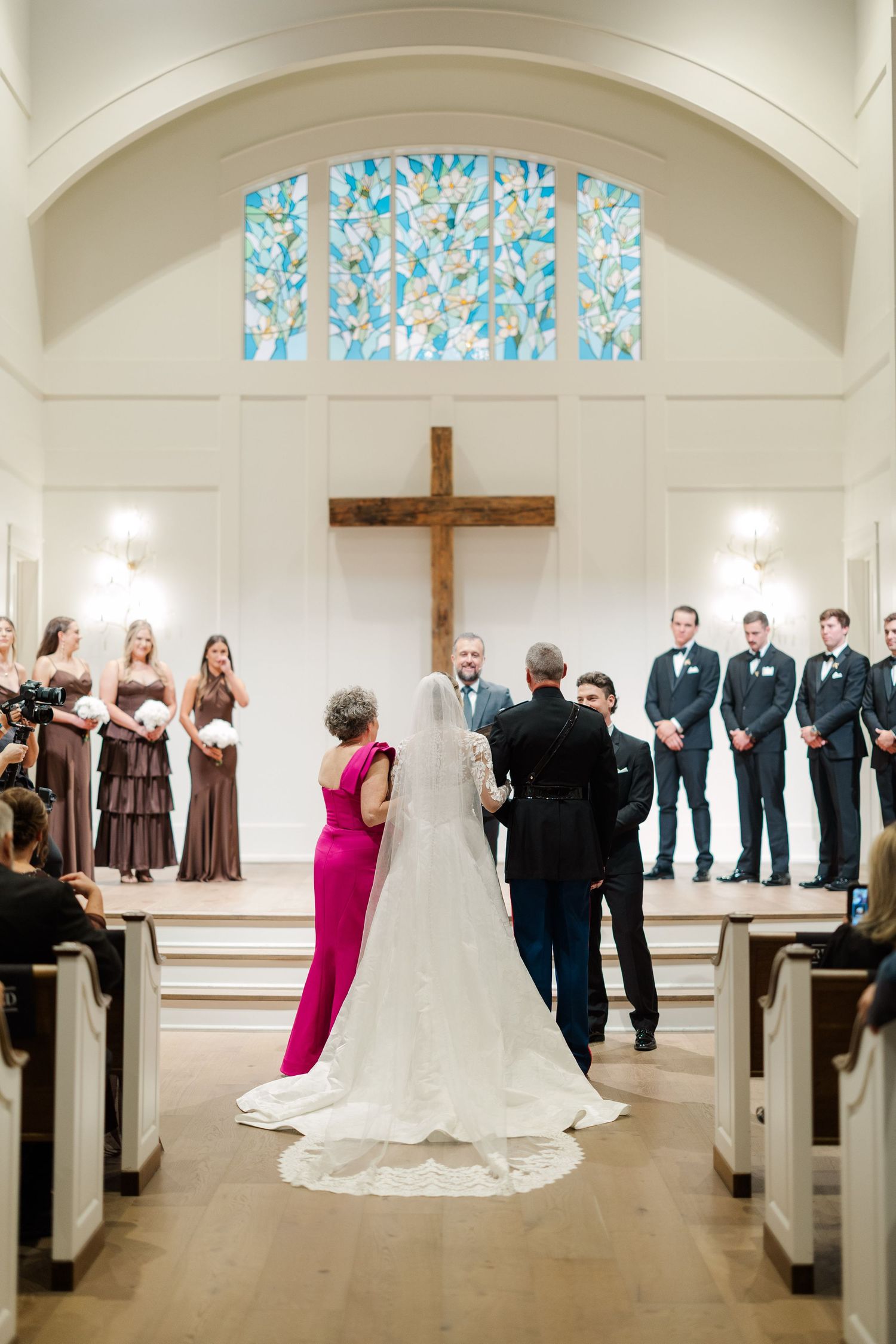 Traditional church wedding ceremony with bridal party and guests in pews under stained glass windows.