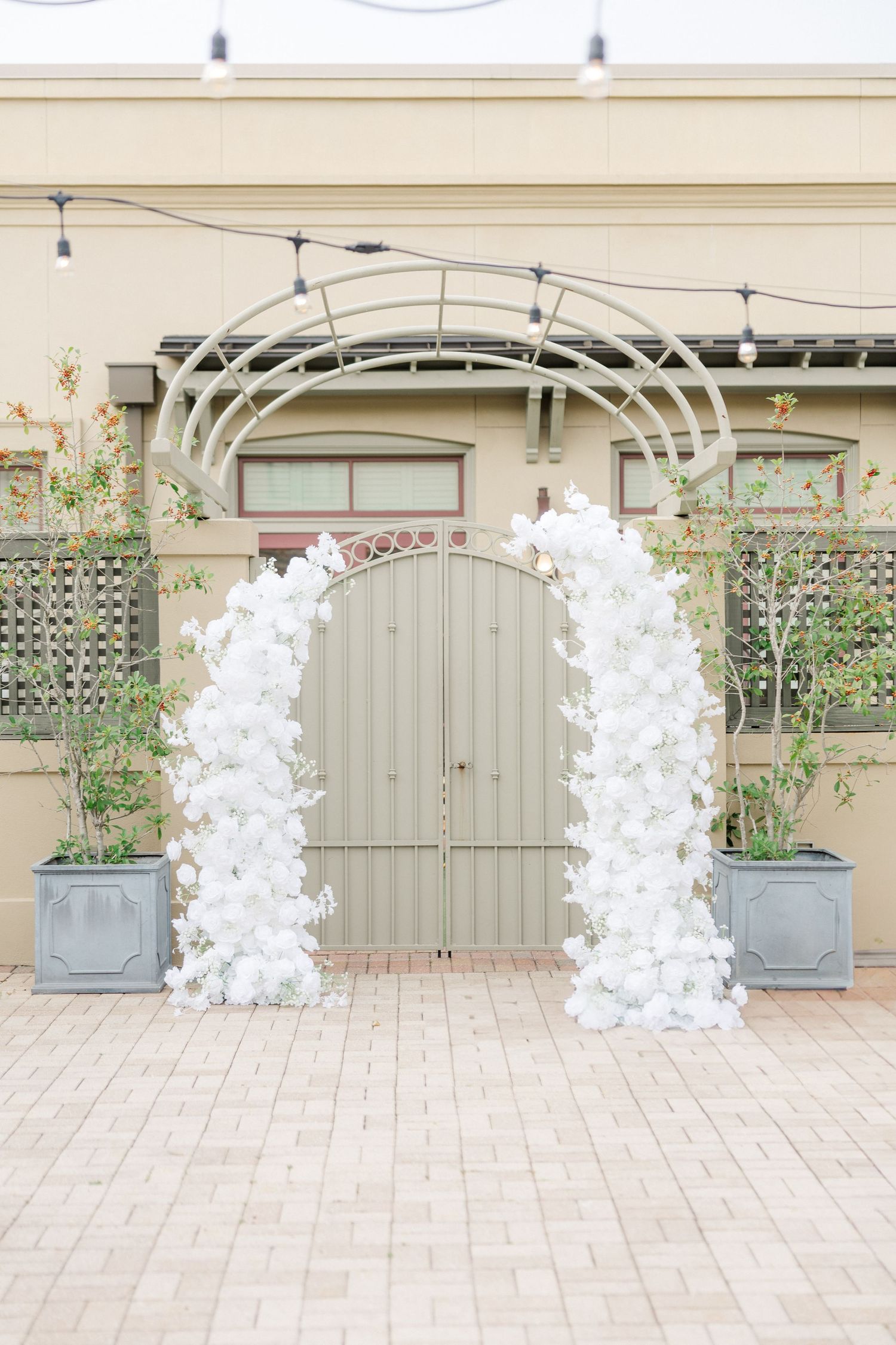 White floral wedding arch with curved metal frame against beige building.