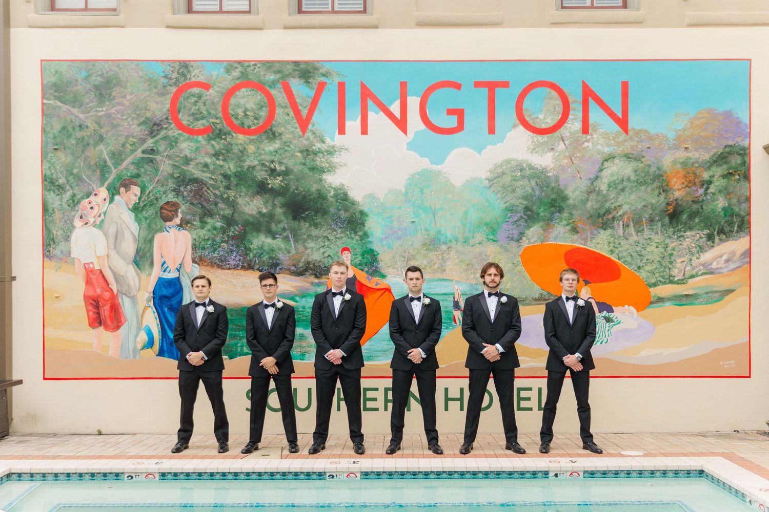 Wedding party poses outdoors in formal attire against a colorful mural backdrop.
