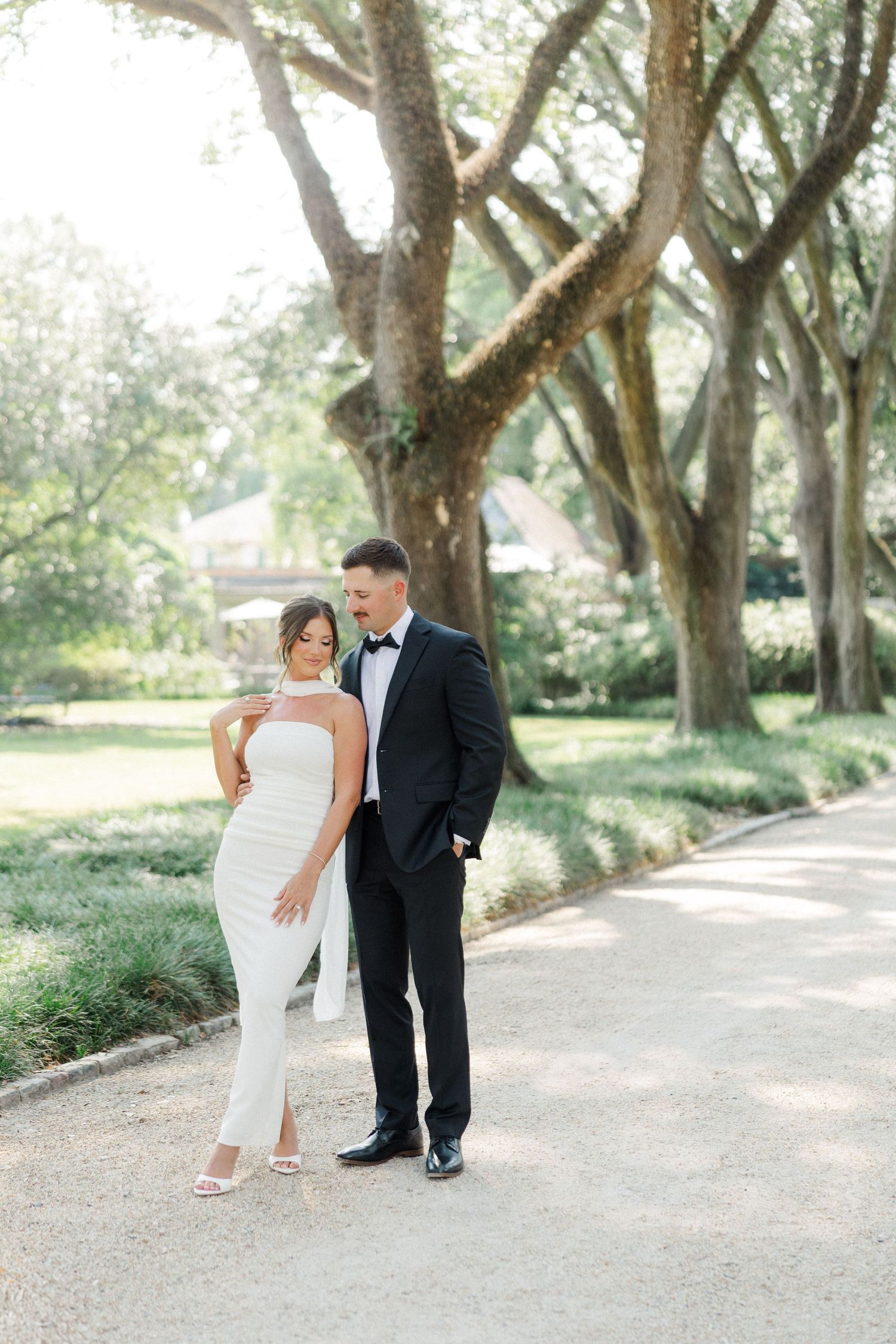 Bride and groom share playful moments while walking along a scenic tree-lined pathway.