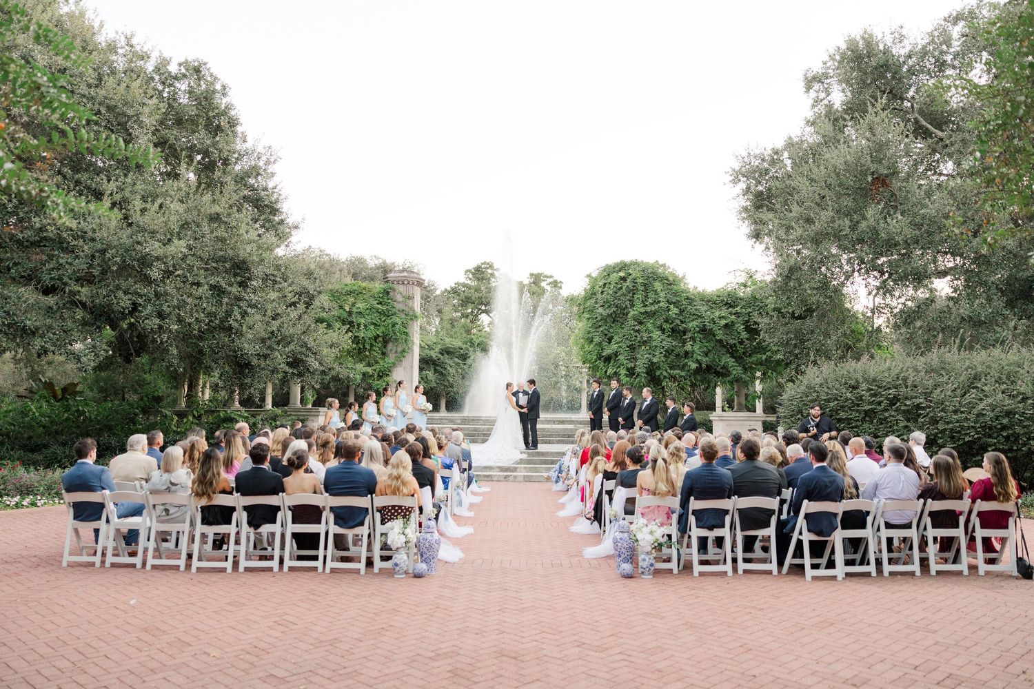 Panoramic view of a garden wedding ceremony with rows of white chairs and natural surroundings.