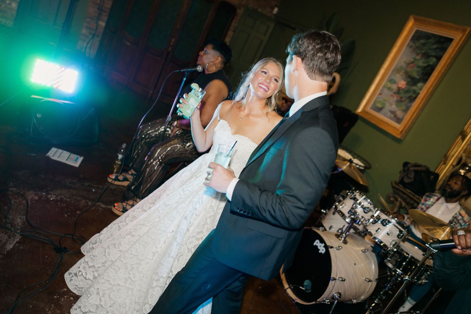Smiling bride and groom toast with champagne glasses near a live band during their wedding reception.