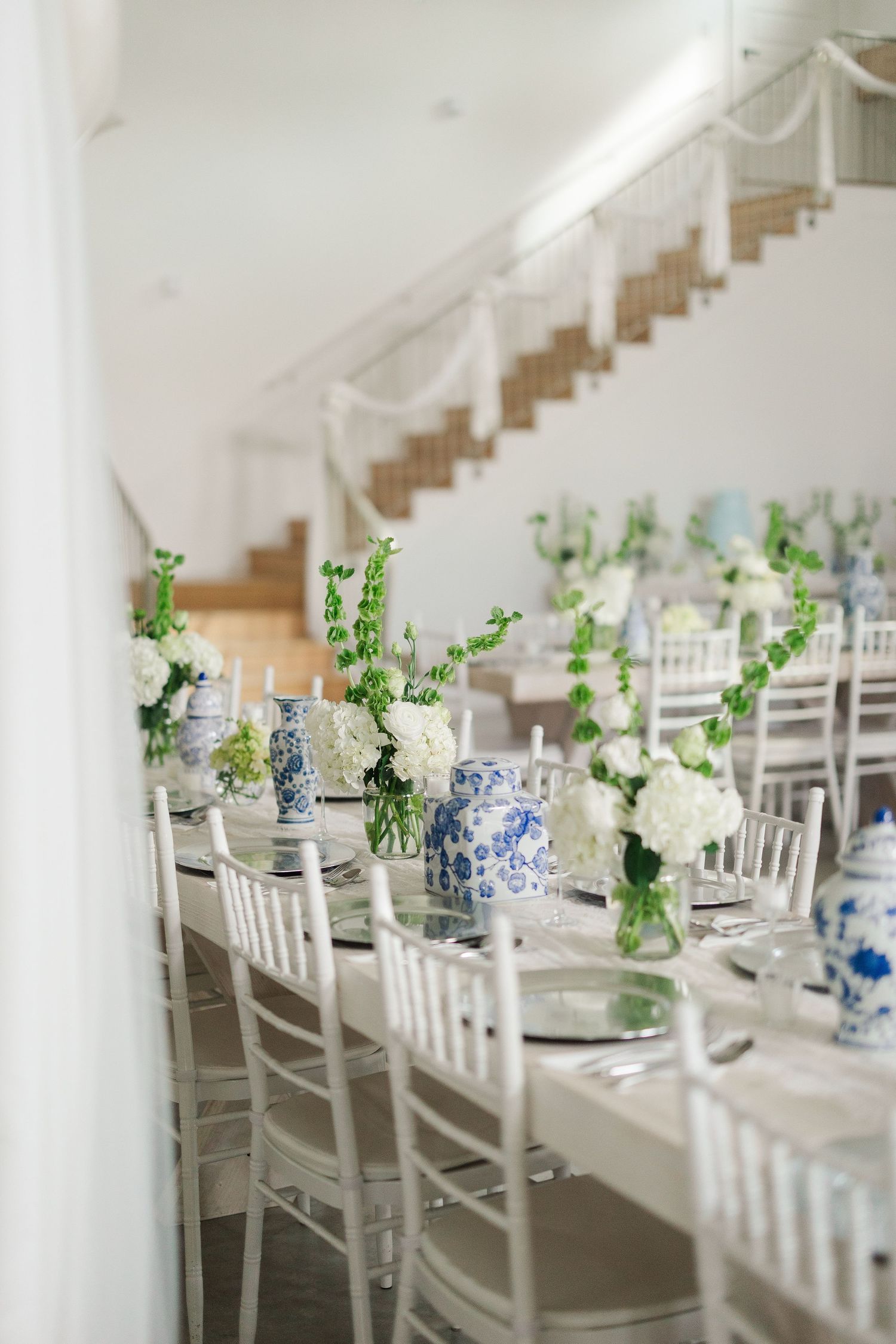 Elegant wedding reception with white chiavari chairs, blue and white chinoiserie vases, and white floral centerpieces.