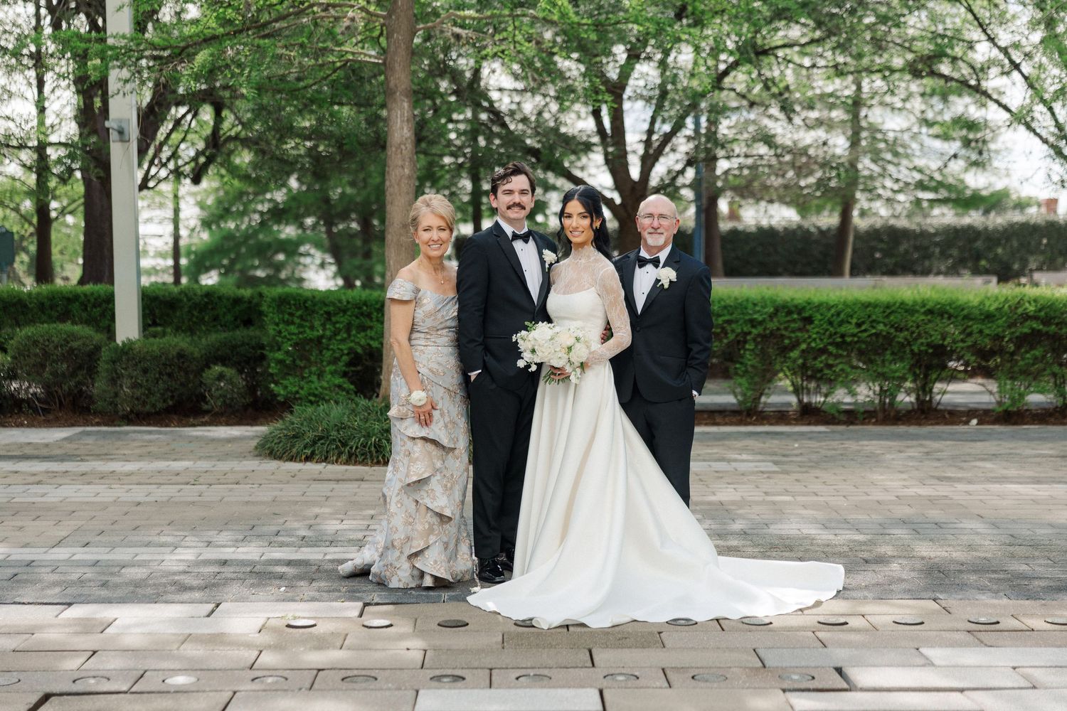 Bride and groom pose with family in formal attire outdoors at elegant wedding venue.