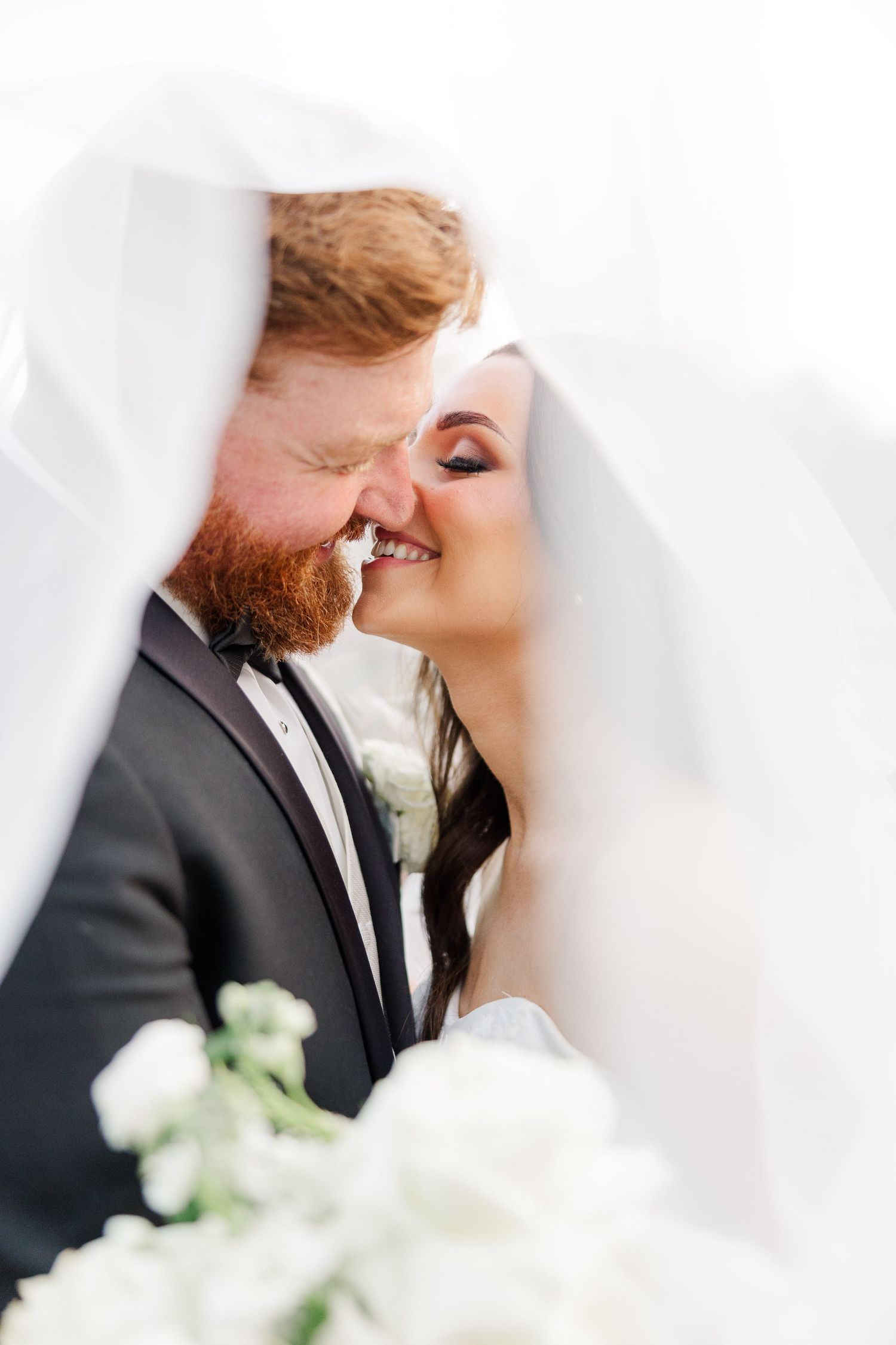 Intimate moment between newlyweds under flowing white veil.