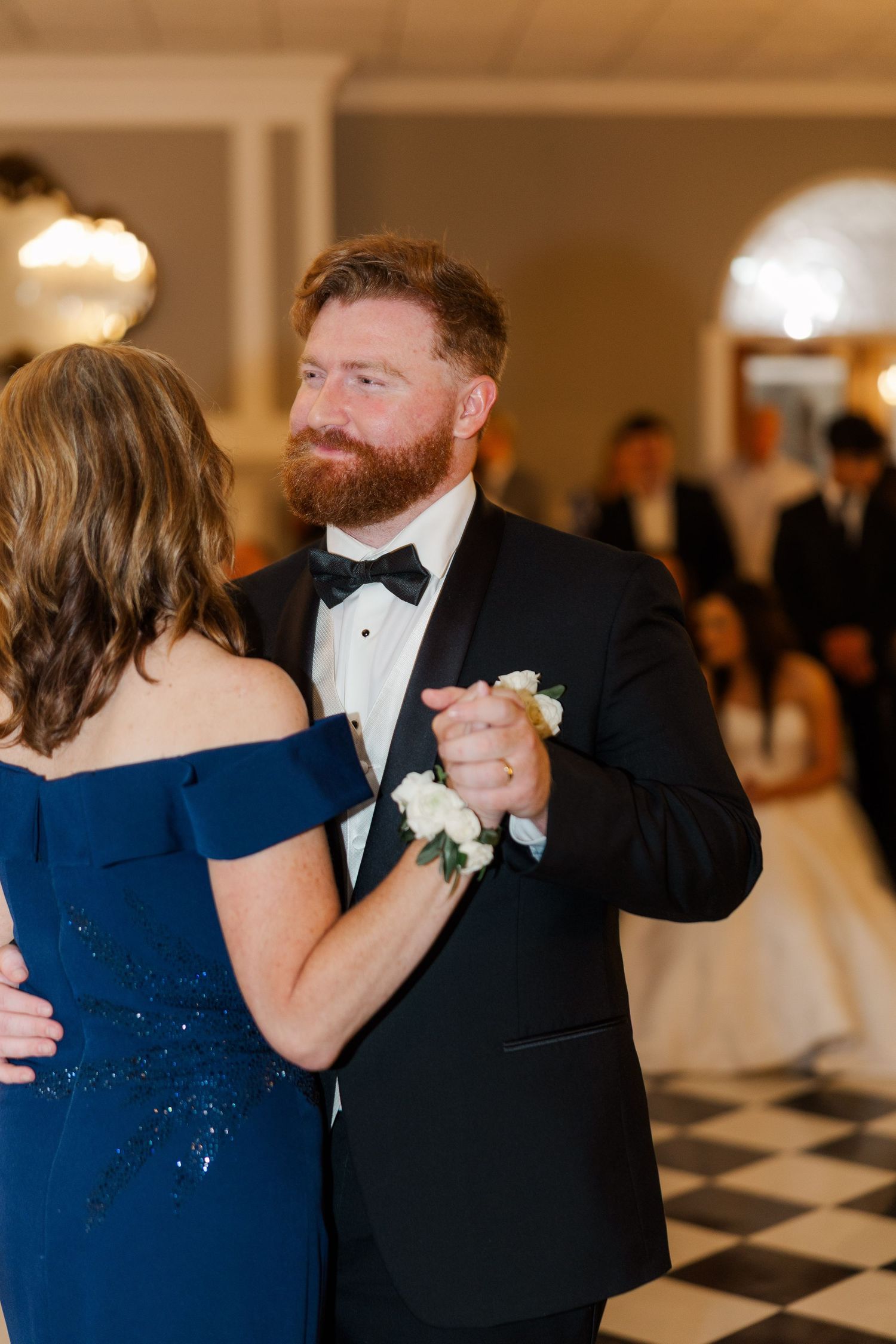 A couple shares a dance on a black and white checkered floor during an elegant wedding reception.