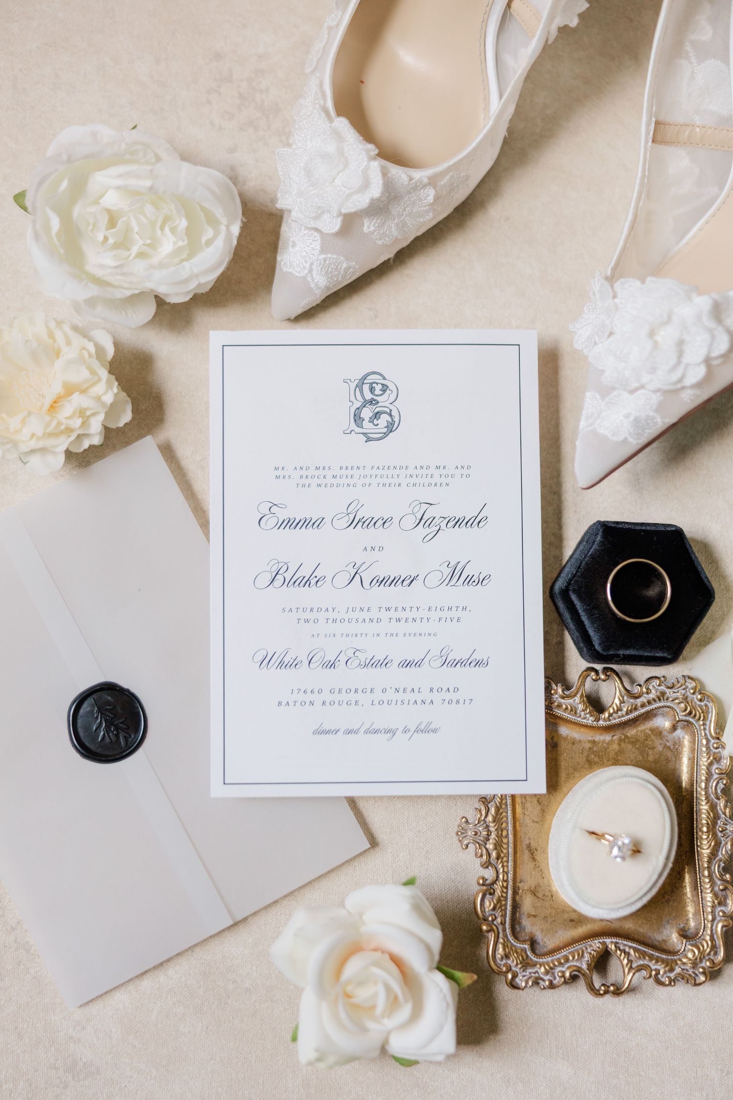 Elegant wedding stationery with white roses and wax seals arranged on a cream surface with ornate gold frames.