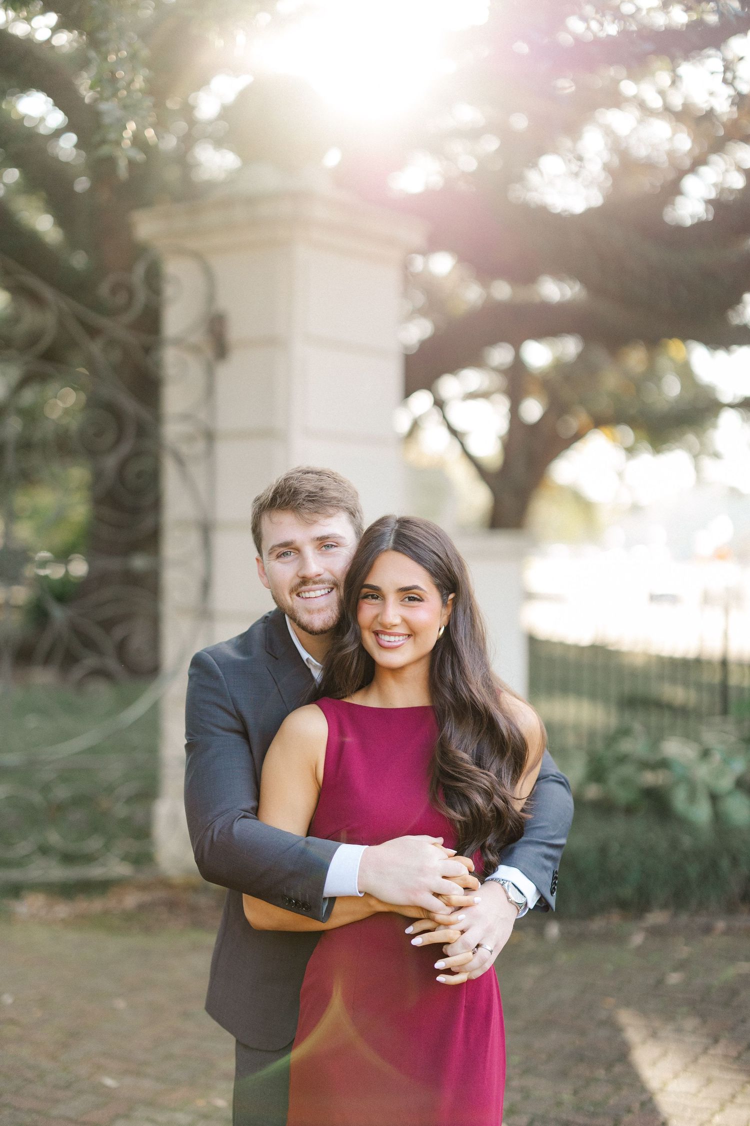 A couple embraces in a romantic outdoor photoshoot with golden sunlight filtering through trees.