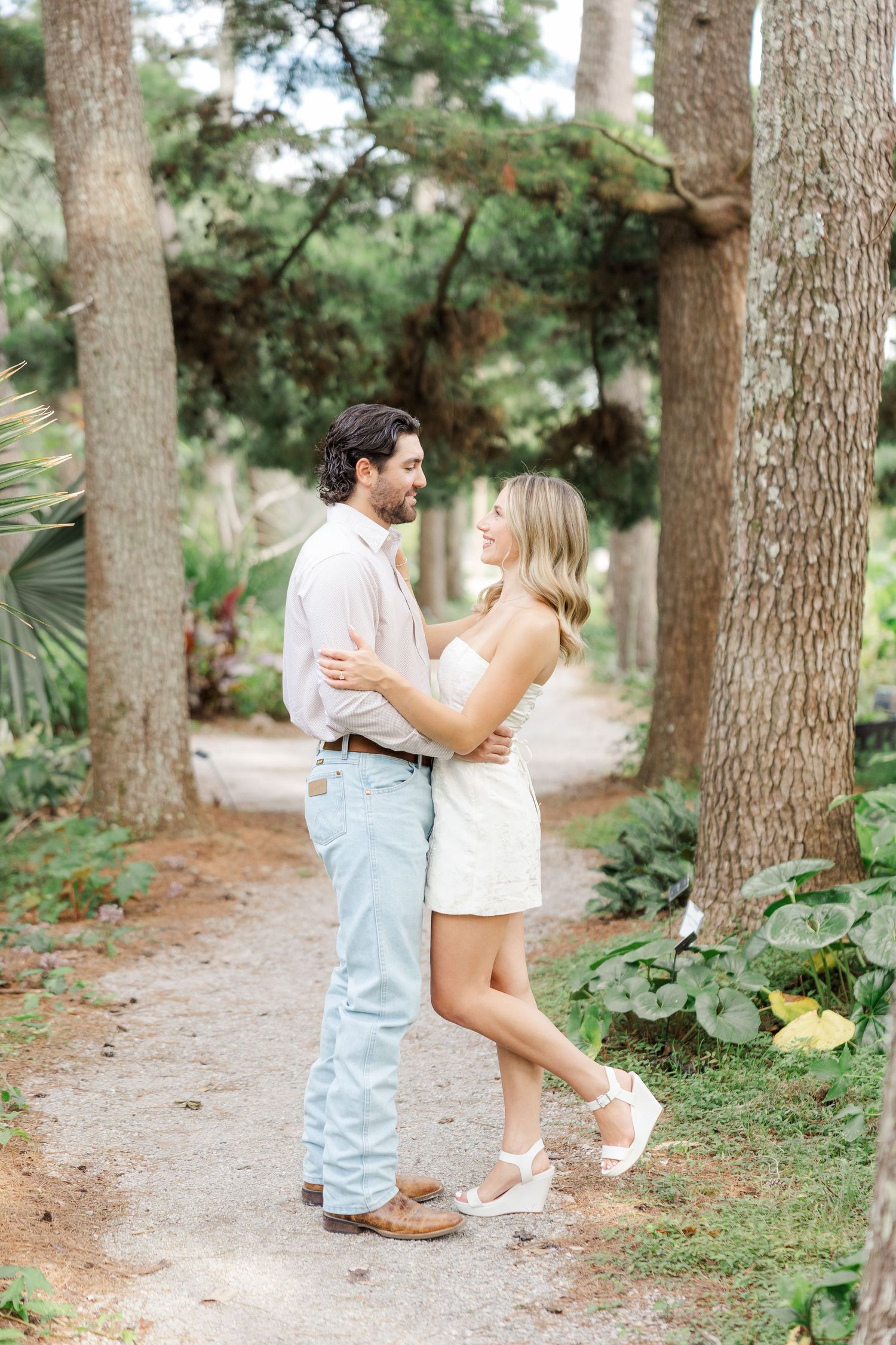 A couple shares playful moments together on a tree-lined path during a romantic outdoor photoshoot.