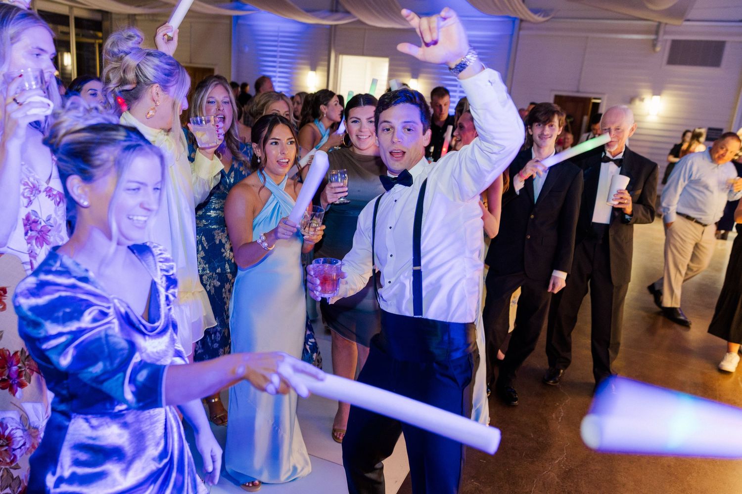 Wedding party dancing under blue lights with hands in the air.
