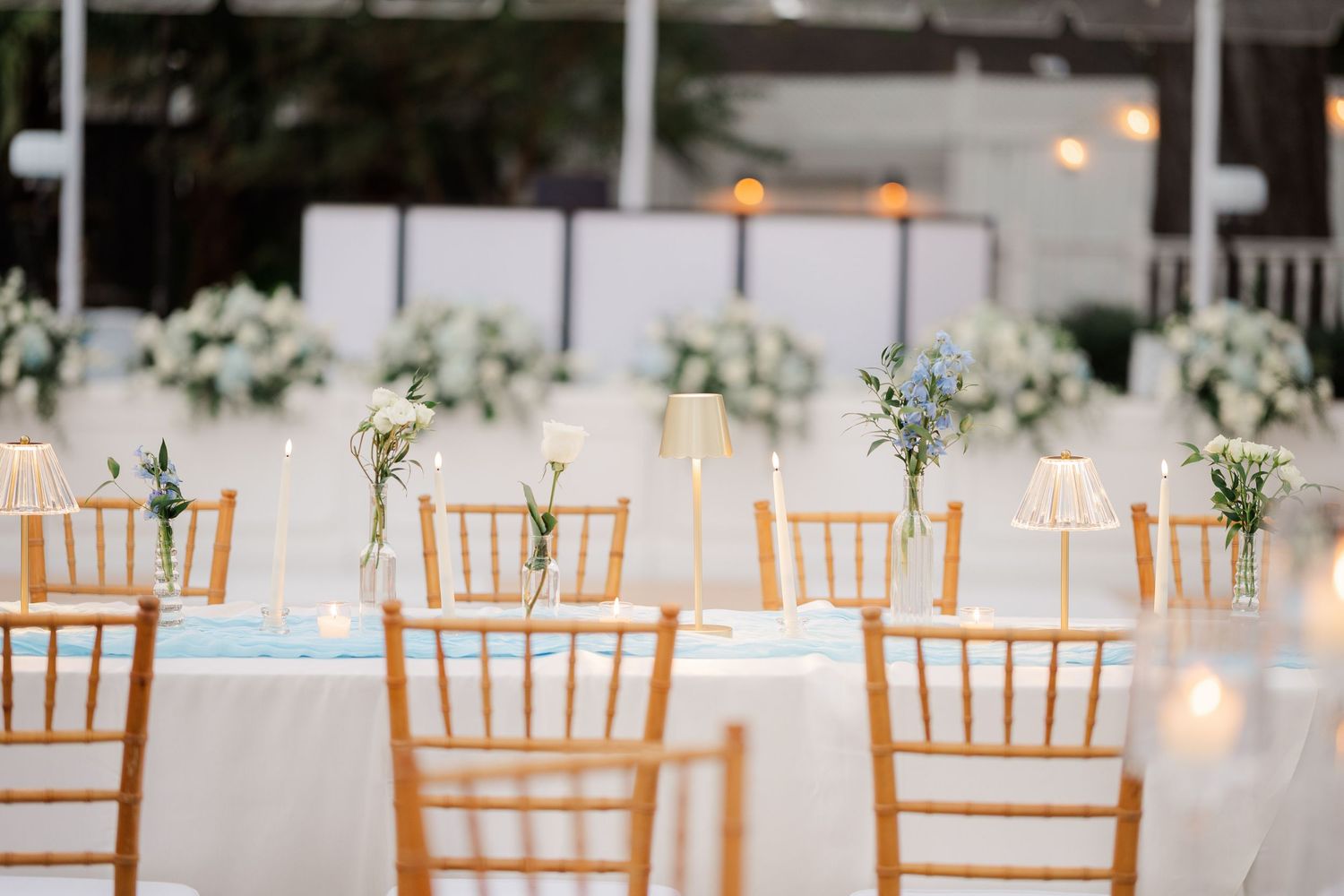 Row of wooden chiavari chairs set up for an elegant wedding reception with white table linens.