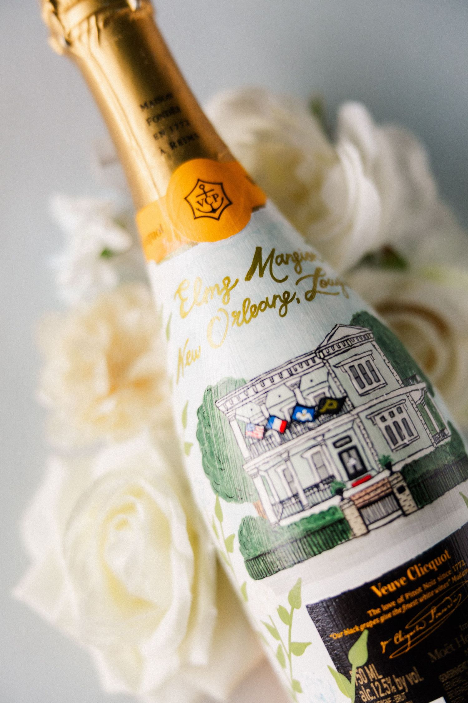 Decorative champagne bottle with custom label featuring an illustrated building design next to white roses.