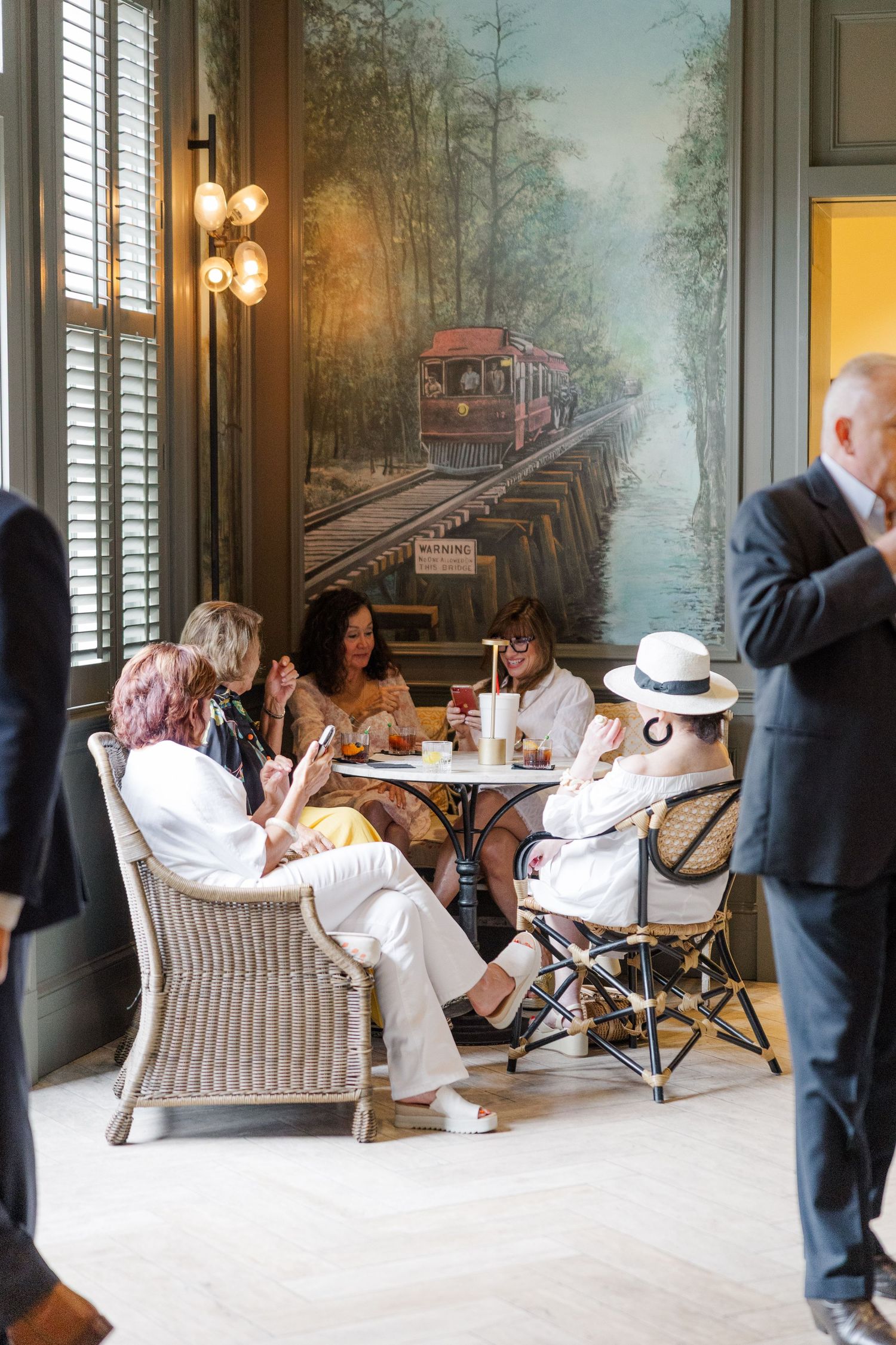 Guests relax in elegant lounge chairs against a scenic mural backdrop at an upscale venue.