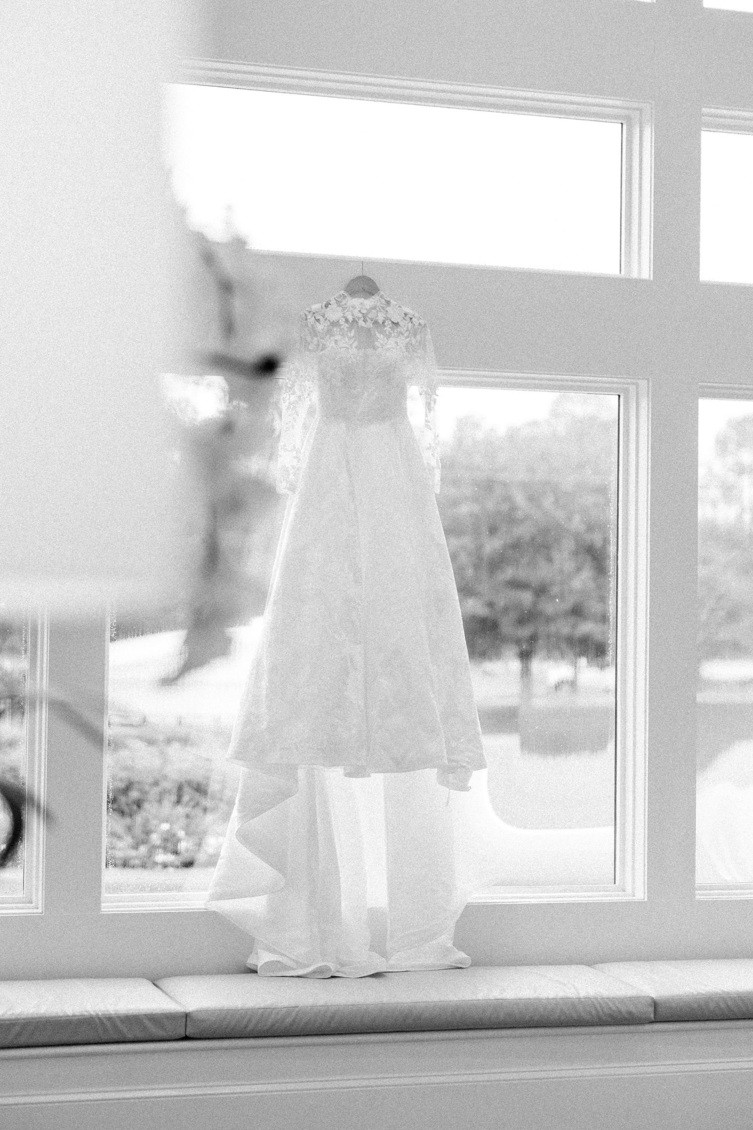 A soft black and white photograph shows a flowing wedding dress silhouette against a bright window.