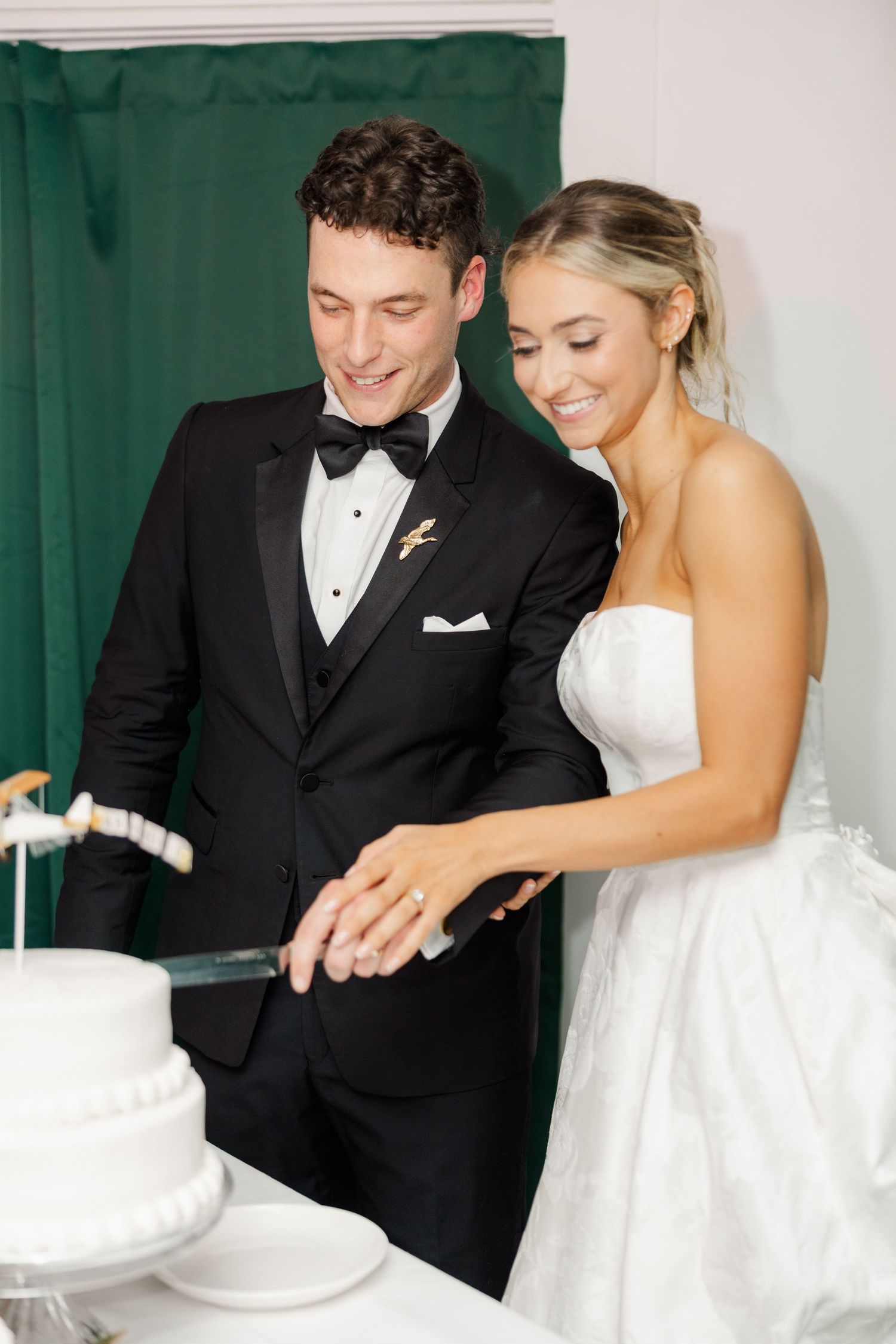 Newlyweds in formal attire cut their white wedding cake together.