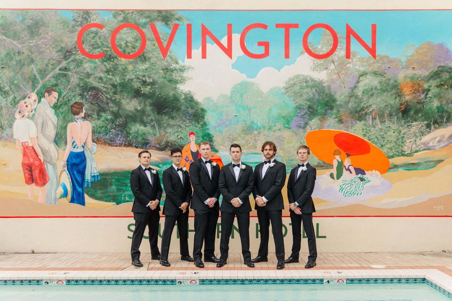 Wedding party in formal attire poses along colorful wall with Covington text at outdoor venue.