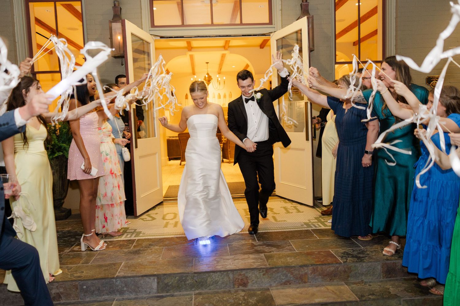 Wedding party celebration exit with guests waving sparklers outside venue at night.