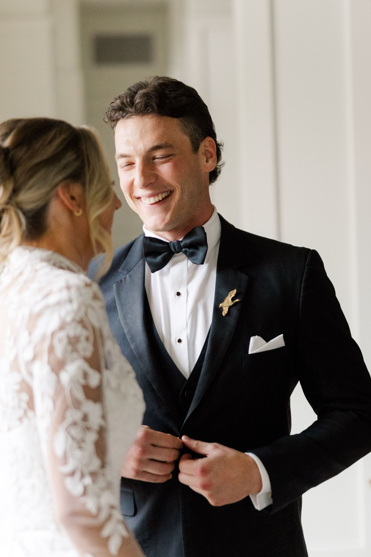 A couple shares a joyful first look moment before their wedding ceremony in a bright hallway.