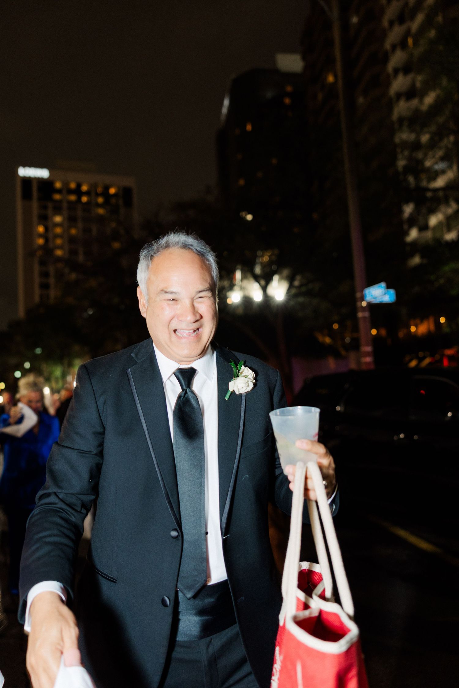 Man in tuxedo holding party favors during nighttime wedding celebration.