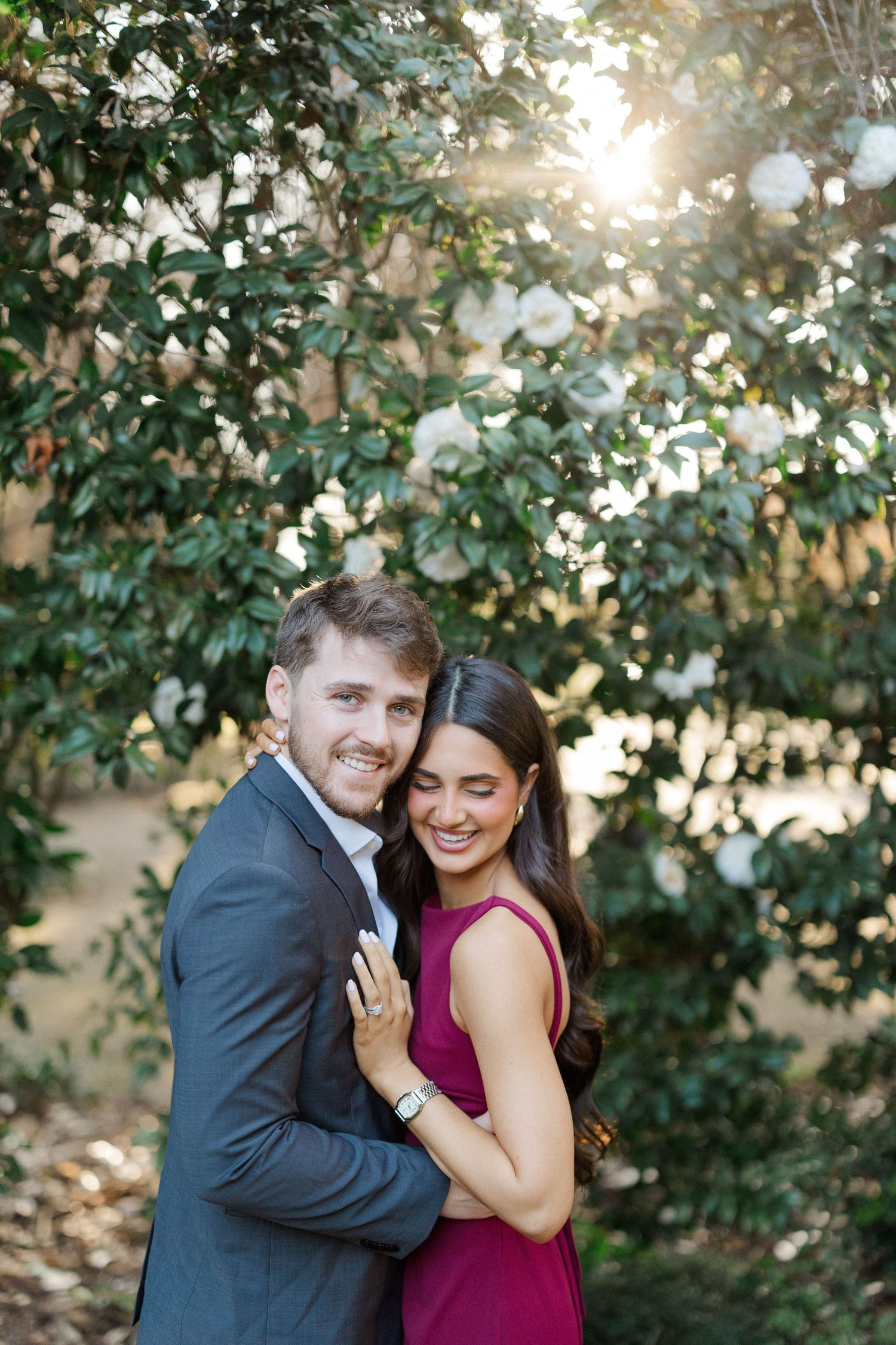 Happy couple embraces outdoors with sunlight filtering through trees behind them.