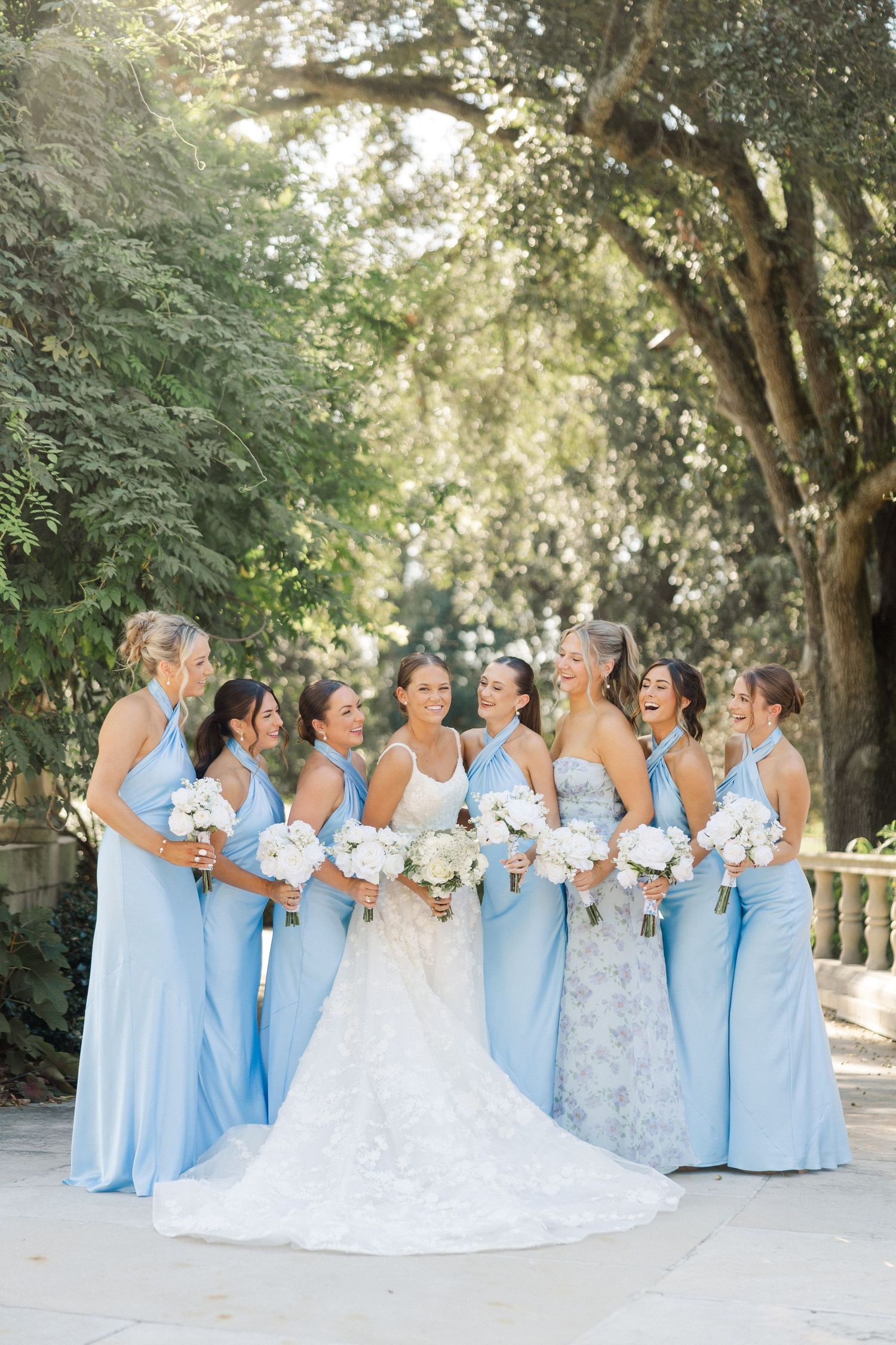 Bridal party in light blue dresses gathered together for outdoor garden photos.