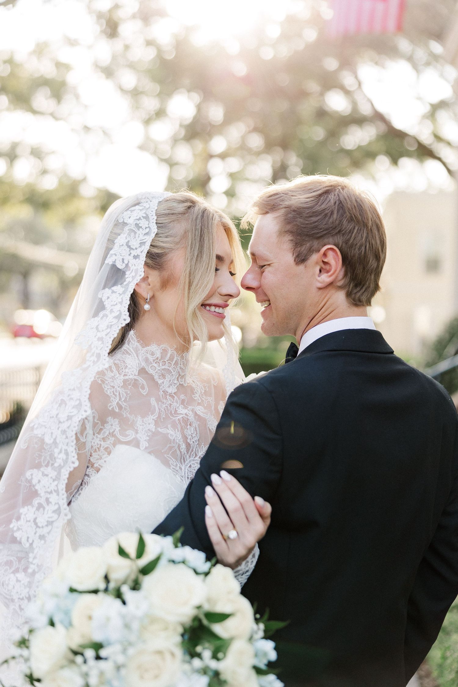 A romantic wedding moment captured in soft sunlight with white floral bouquet details.