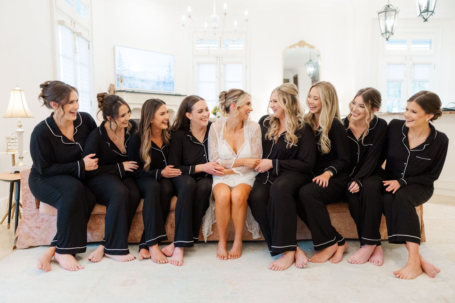 A group of dancers in black leotards sit in a line along a white studio wall during dance class.